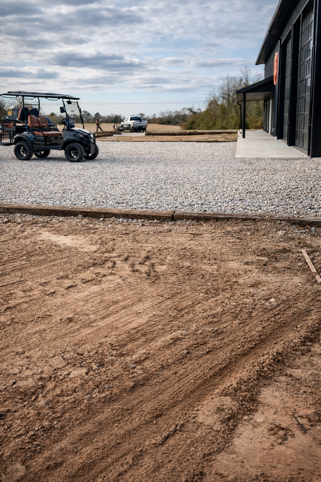 Clean  gravel parking lot located in Jack Alabama next to a black building with a golf cart and pickup truck parked nearby, with a cloudy sky and open field in the background.