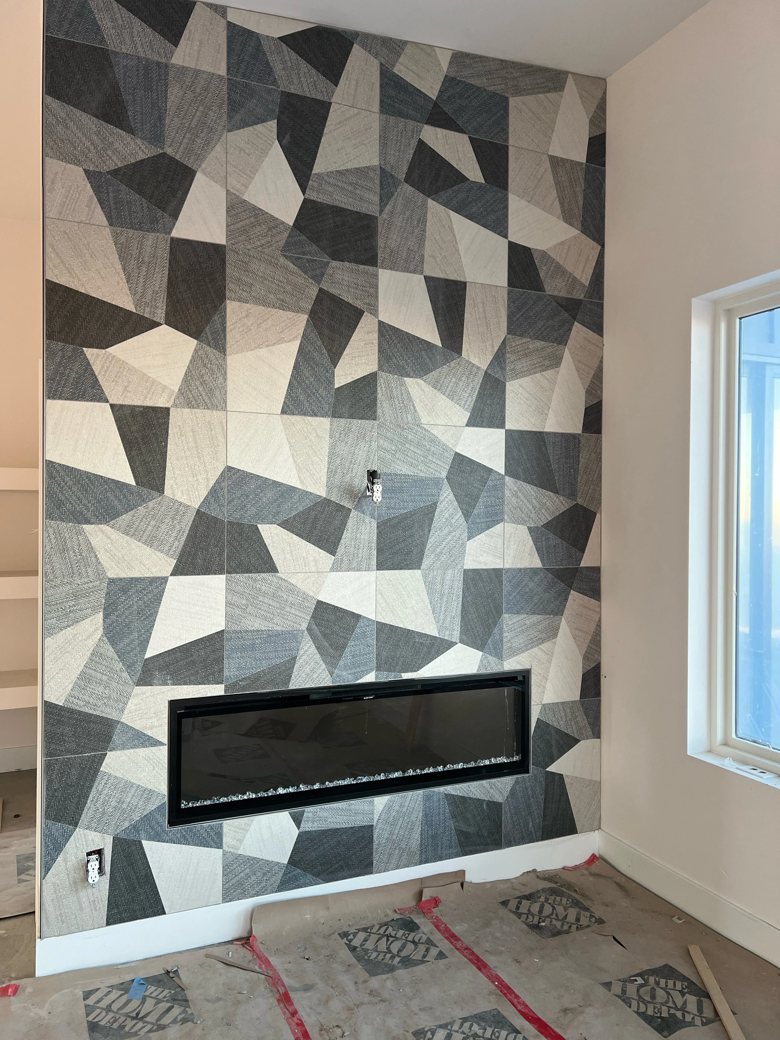 Interior fireplace feature wall with geometric tile finish during residential construction.