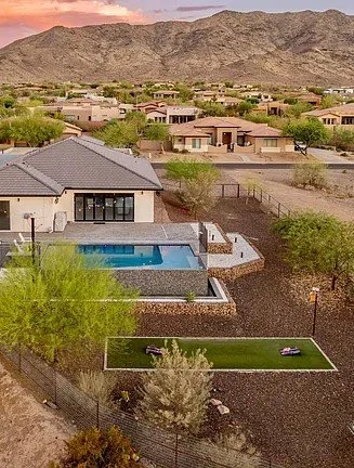 Residential backyard with pool, gabion walls, turf, fencing, and desert landscaping.