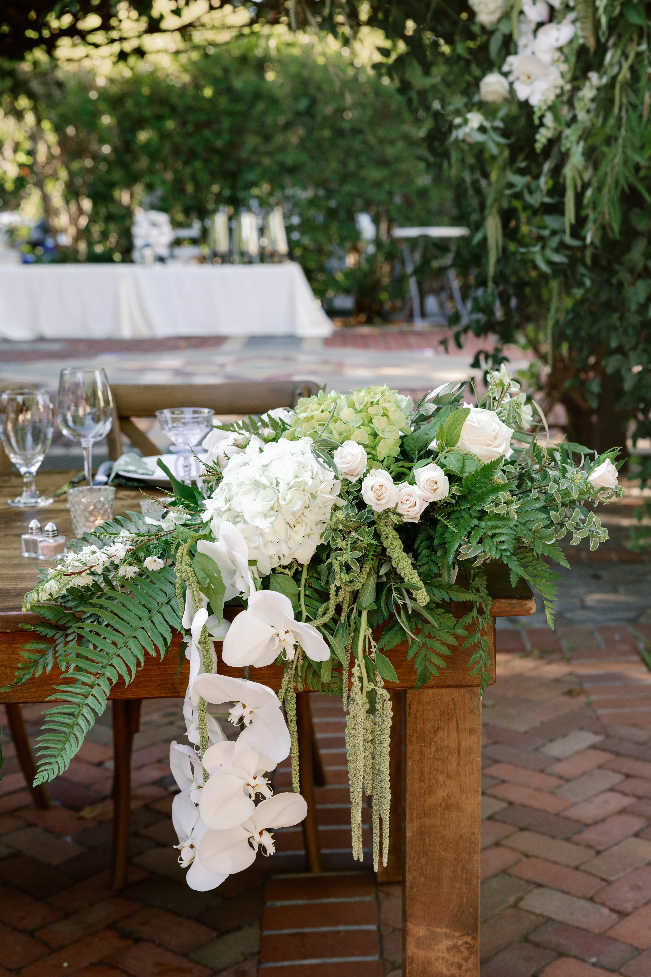 Image of the sweetheart table arrangement with white cascading orchids, hydrangea, roses, Amaranthus, and ferns.