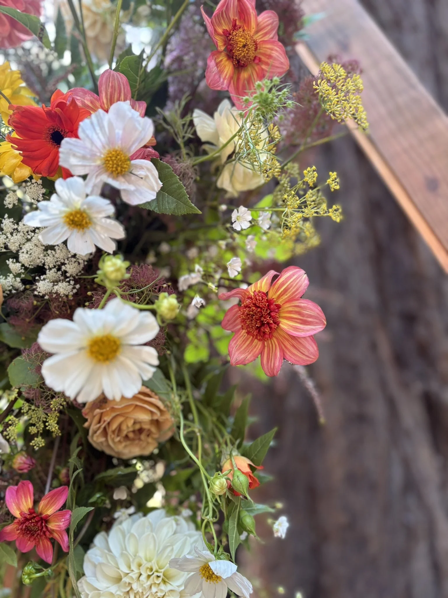 Detail image of summer time wild flowers of cosmos, dahlias, roses, and some greenery.
