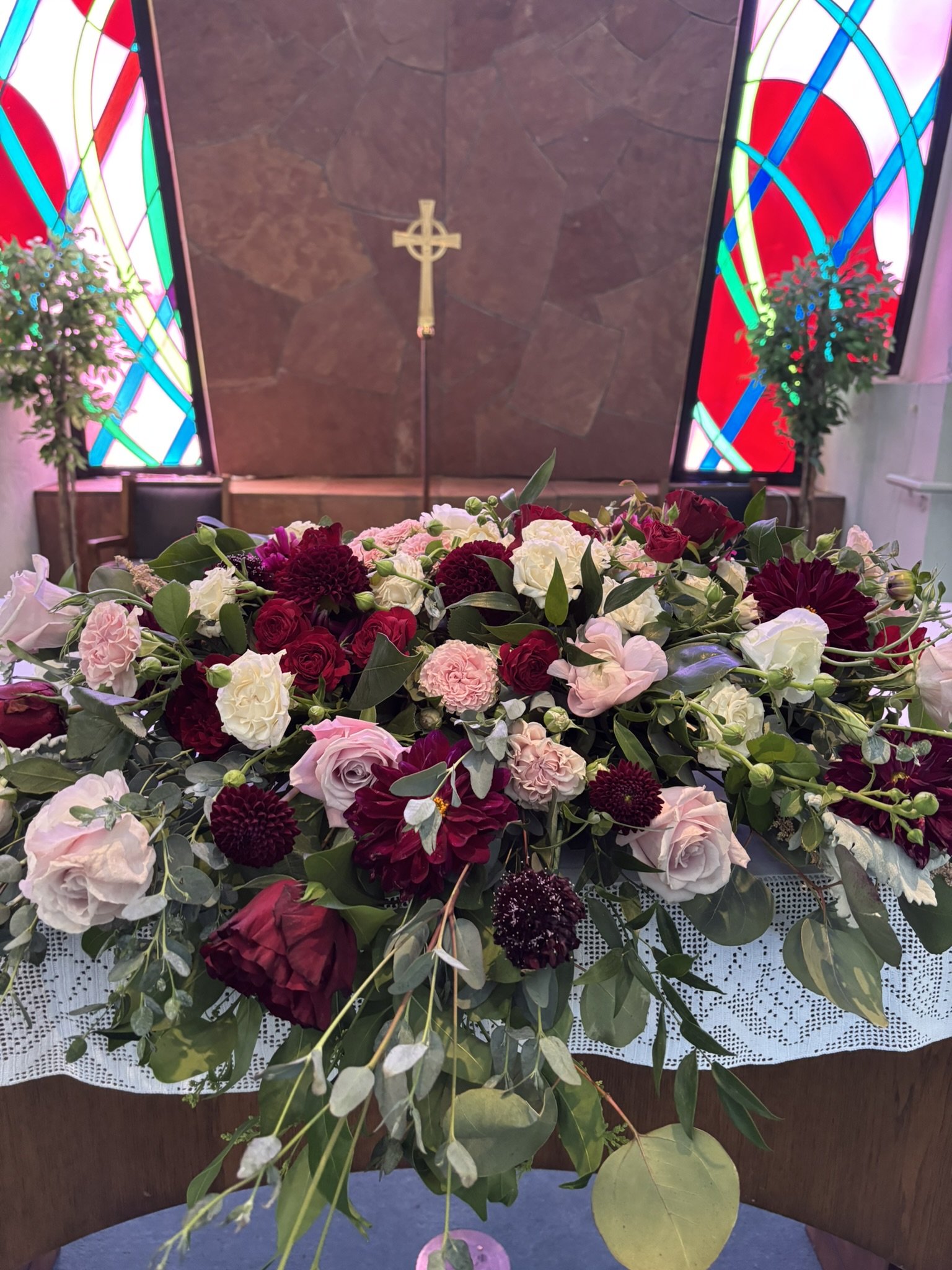 Church alter flower arrangement of cream, pink, and burgundy roses.