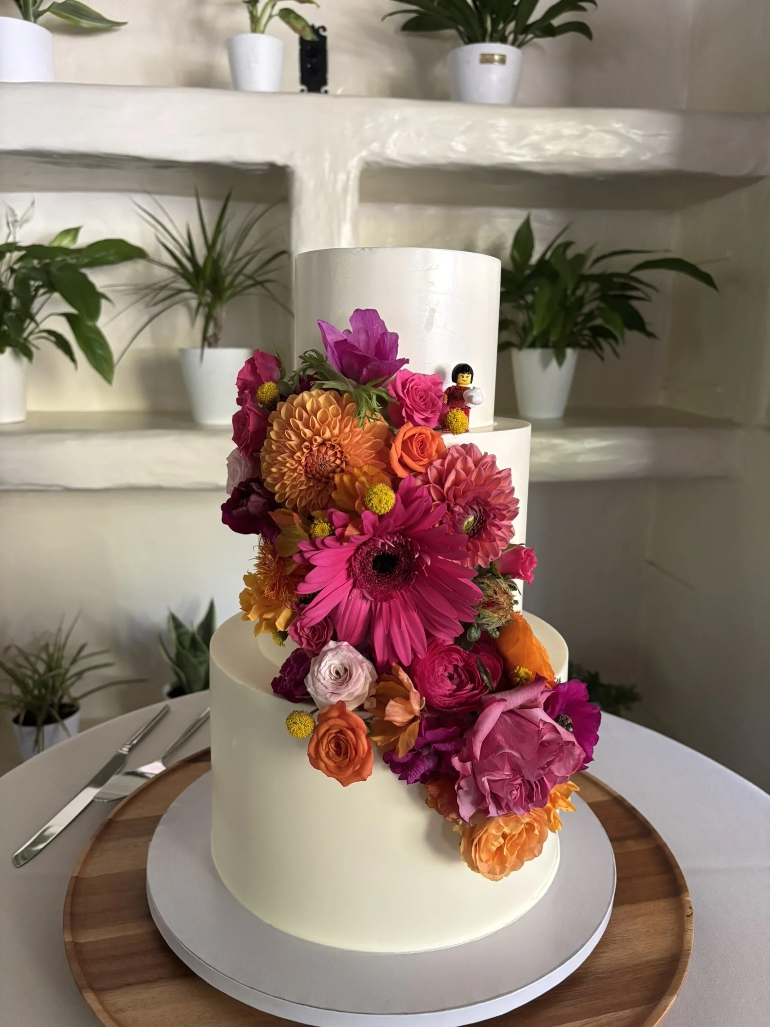 Image of the wedding cake with flowers cascading down the side. Orange dahlias, fuchsia gerberas, and colorful sprig roses.