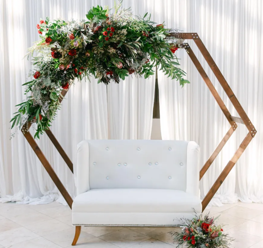 Hexagon wedding arch with floral arrangement and white love seat. Flower arrangement have burgundy roses, succulents and protea.