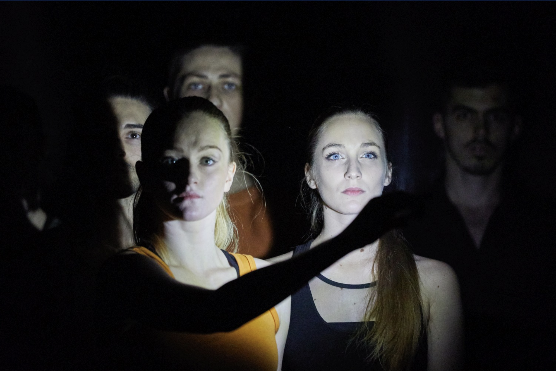 Bardo: dancers' faces emerging from darkness in a narrow beam of light