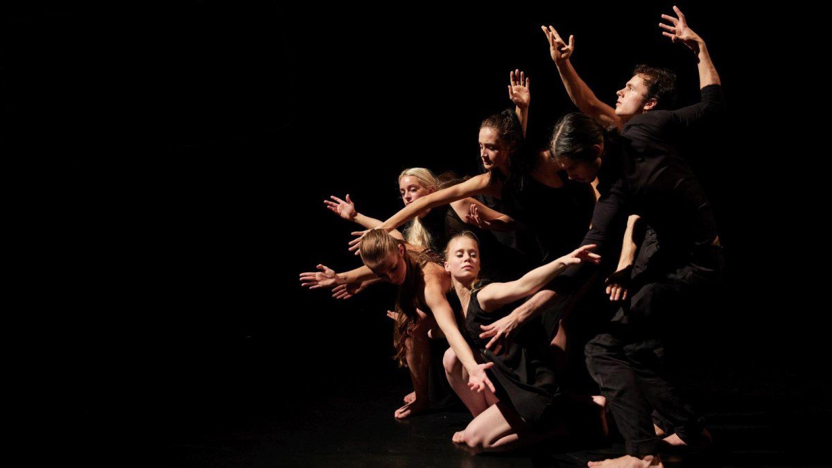 MayFly: an ensemble of dancers reaching upward together on a dark stage