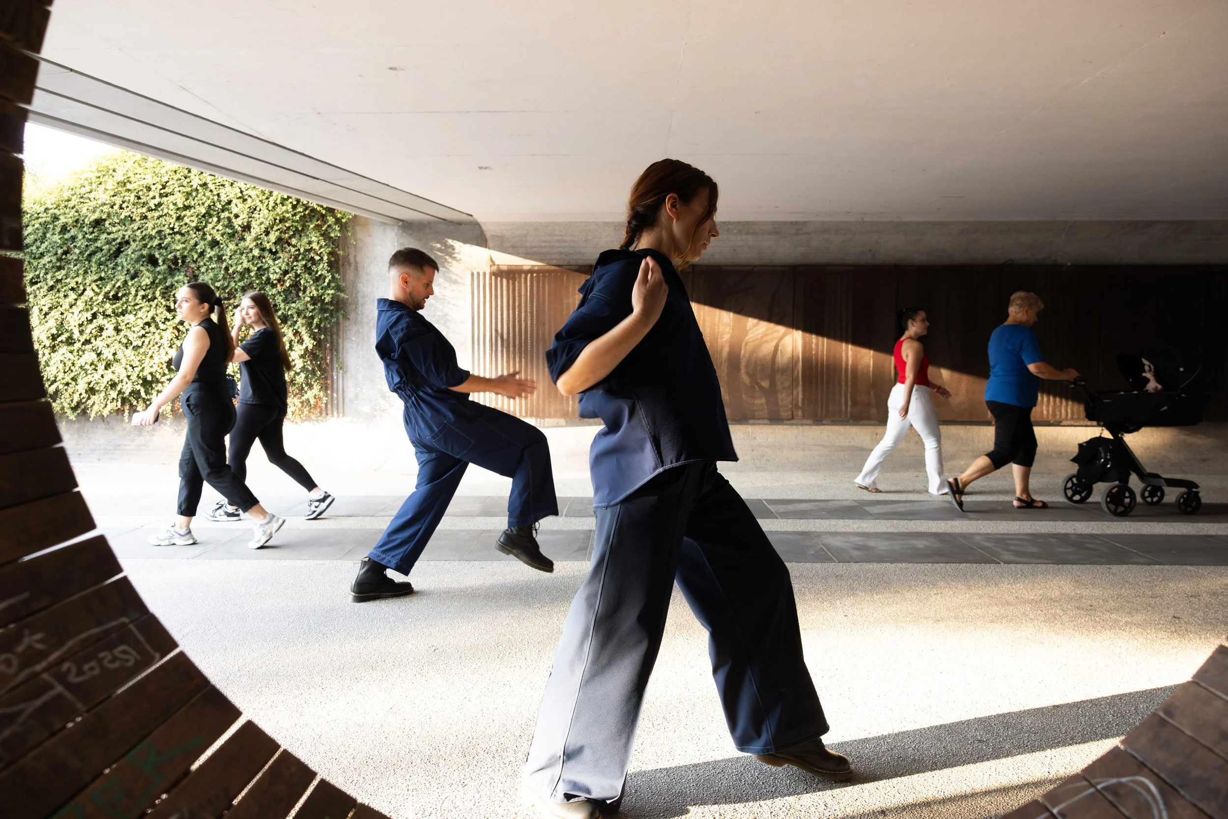 Seagulls Fly Early: two performers walking through a covered passage among passers-by