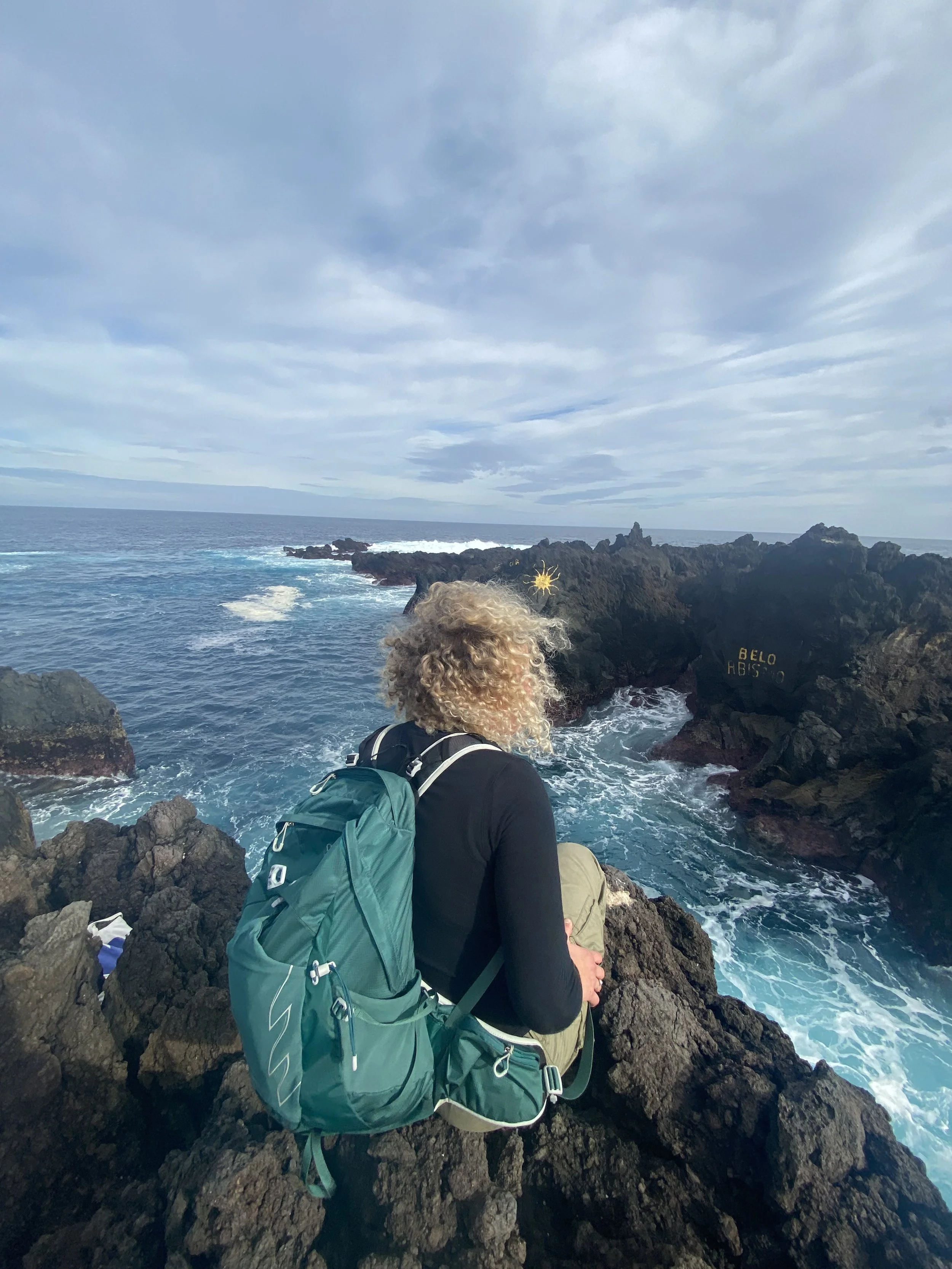 Backpacker sidder på klippe ved havet med rygsækken pakket, omgivet af storslående natur – oplev eventyrlige grupperejser med PERSPEKTIV.