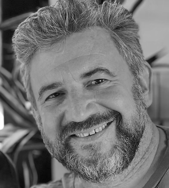Black and white photo of a smiling man with salt-and-pepper hair and beard, looking directly at the camera.
