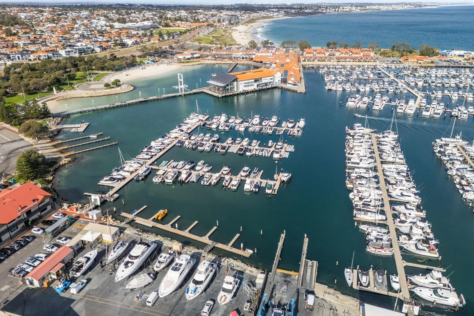 Aerial view of a marina with numerous boats docked, a water park, and surrounding residential area near the coastline.