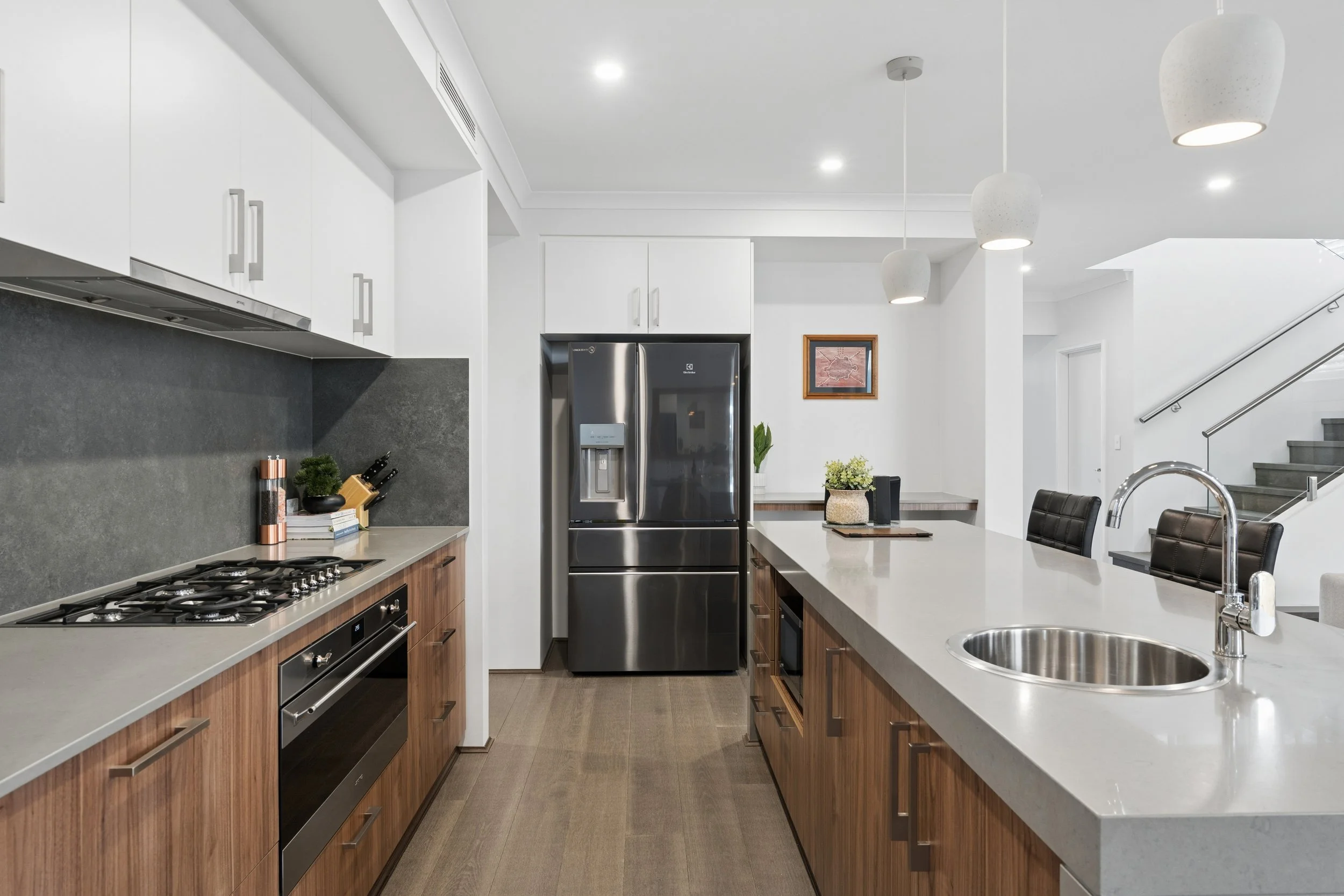 Modern kitchen with white cabinets, stainless steel refrigerator, built-in oven, gas stove, white countertops, and pendant lights.