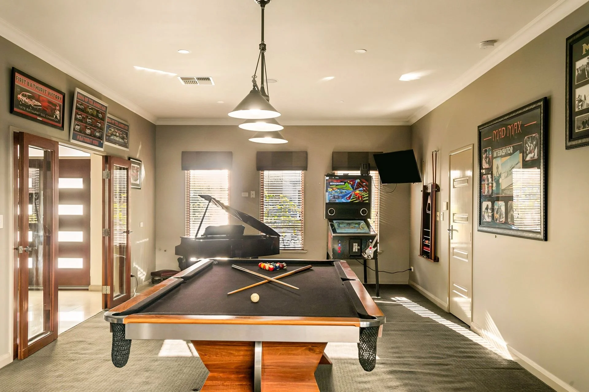 A recreational room with a pool table, a piano, arcade machines, and framed photos and posters on the walls.