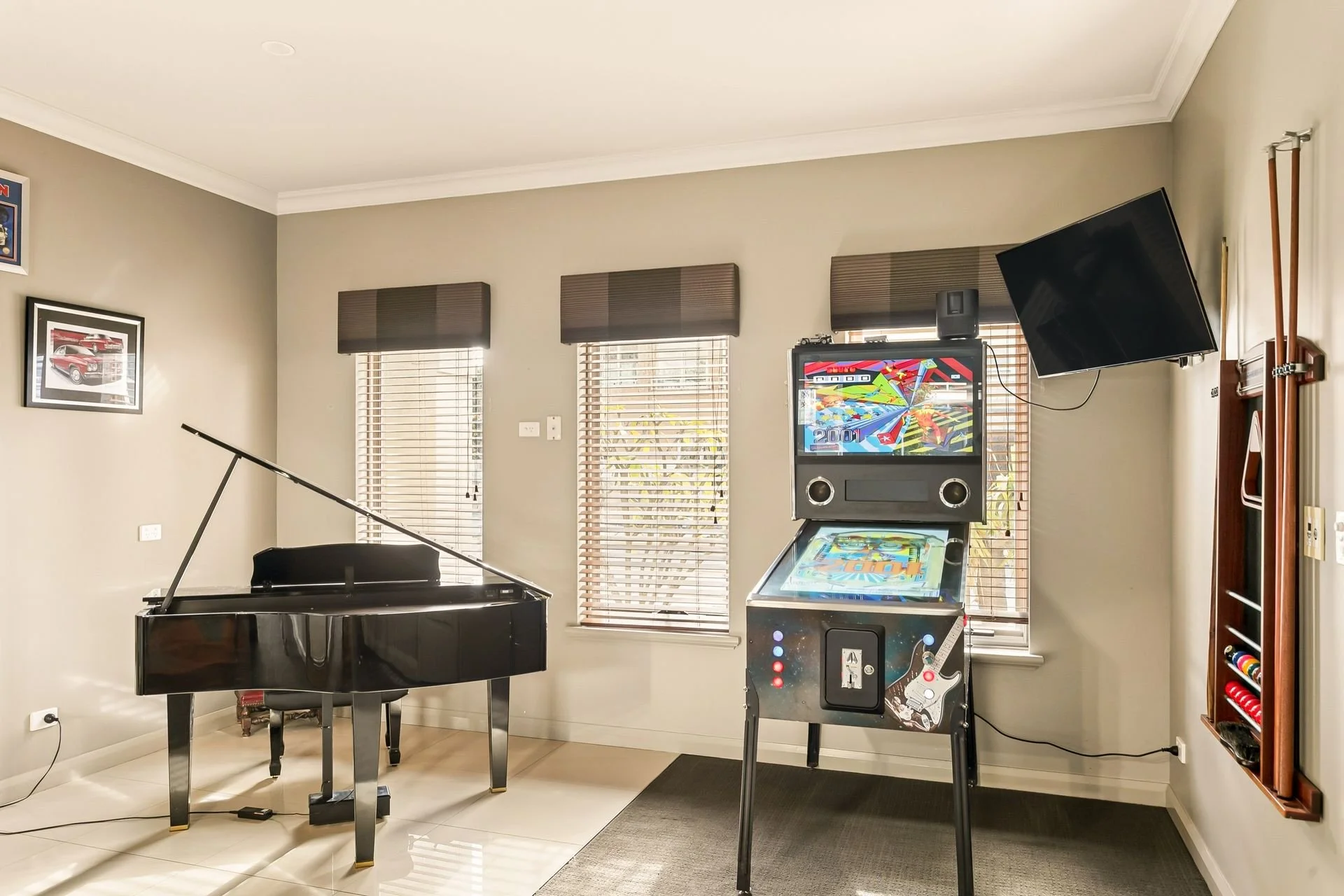 Interior of a room with a black grand piano and a vintage arcade game machine in front of a window with blinds