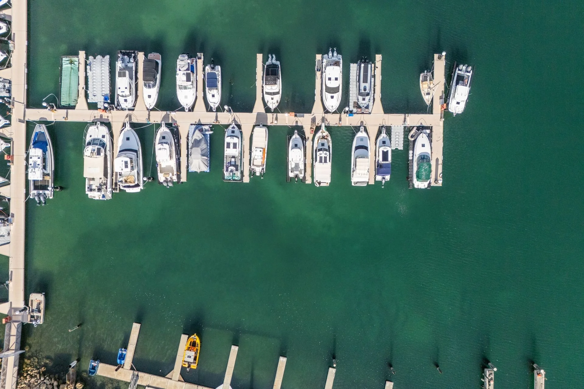 An aerial view of a marina with multiple boats docked along piers extending into greenish water.