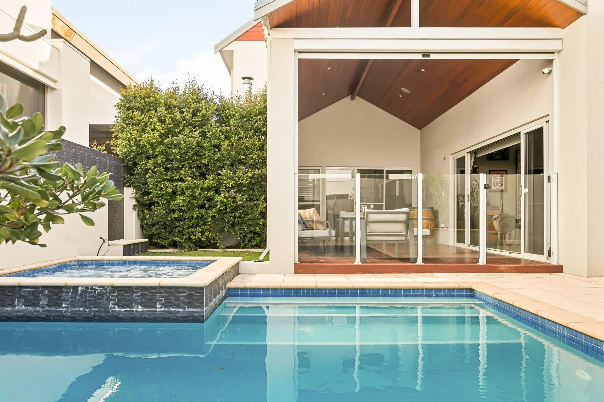 Backyard with swimming pool and outdoor living space featuring sliding glass doors, patio furniture, and lush greenery.