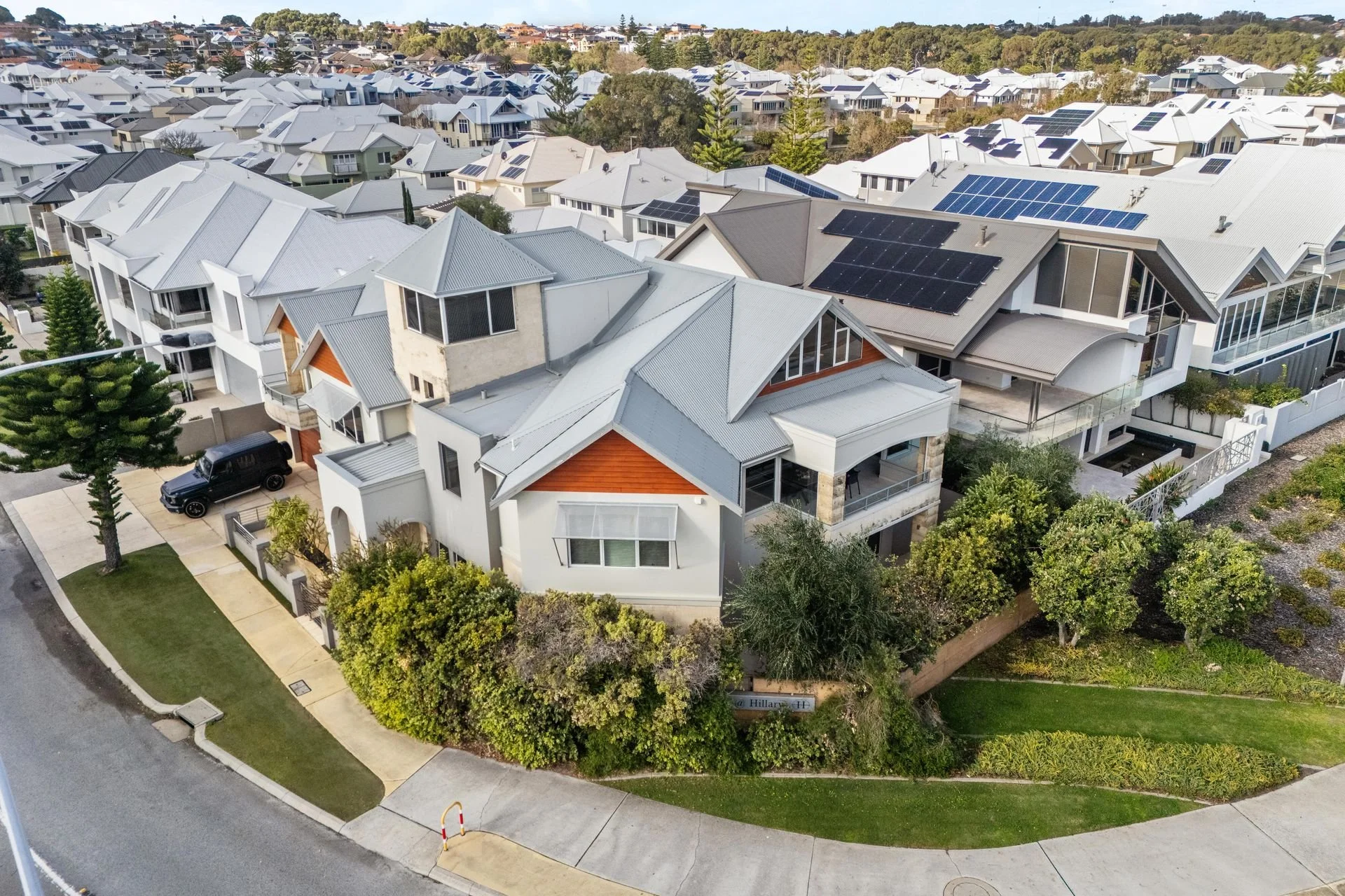 Aerial view of a residential neighborhood with modern houses, many with solar panels on their roofs, surrounded by trees and greenery.