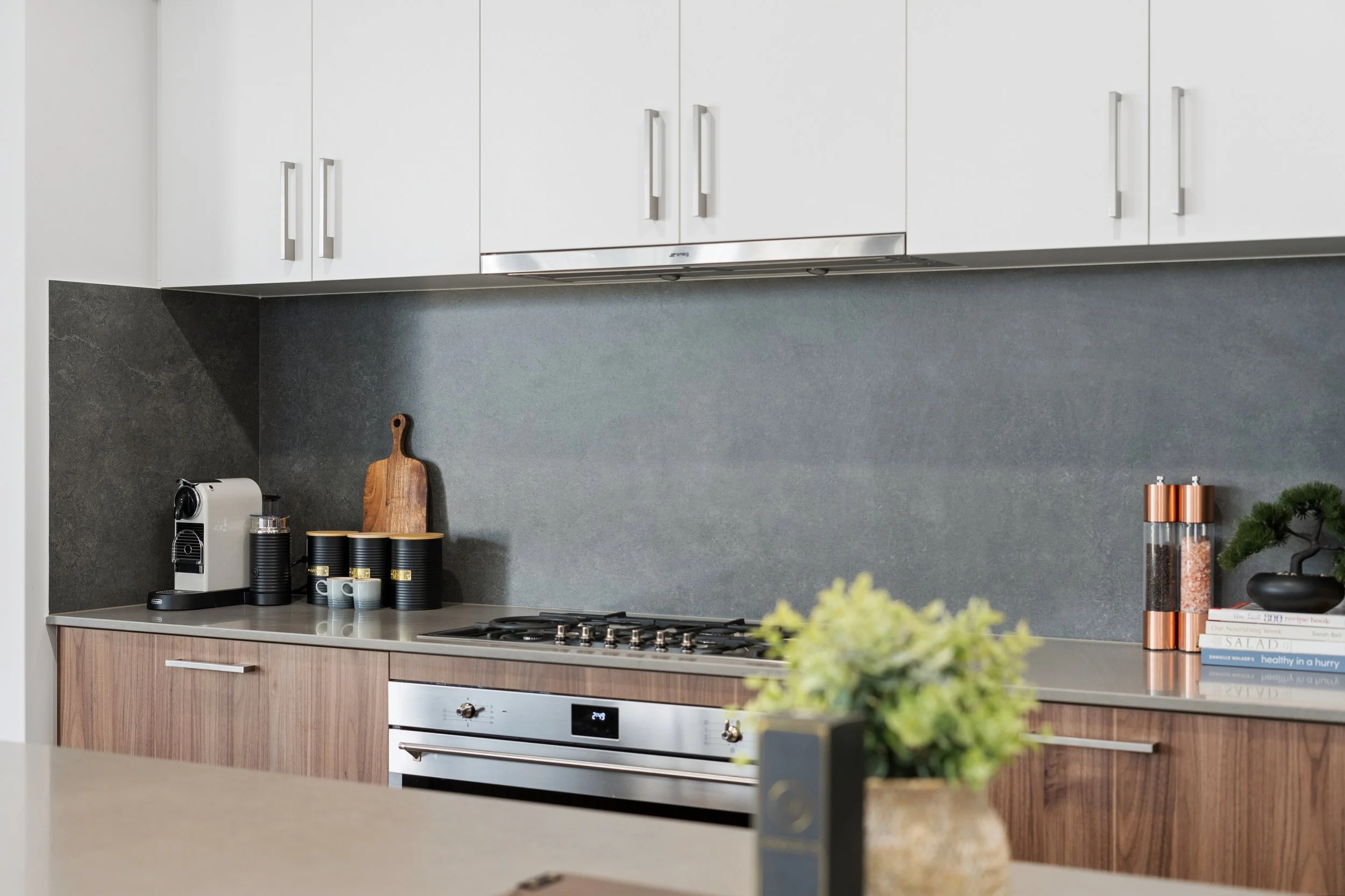 Modern kitchen with white upper cabinets, dark gray backsplash, and wooden lower cabinets, with kitchen appliances and decor on the countertop.