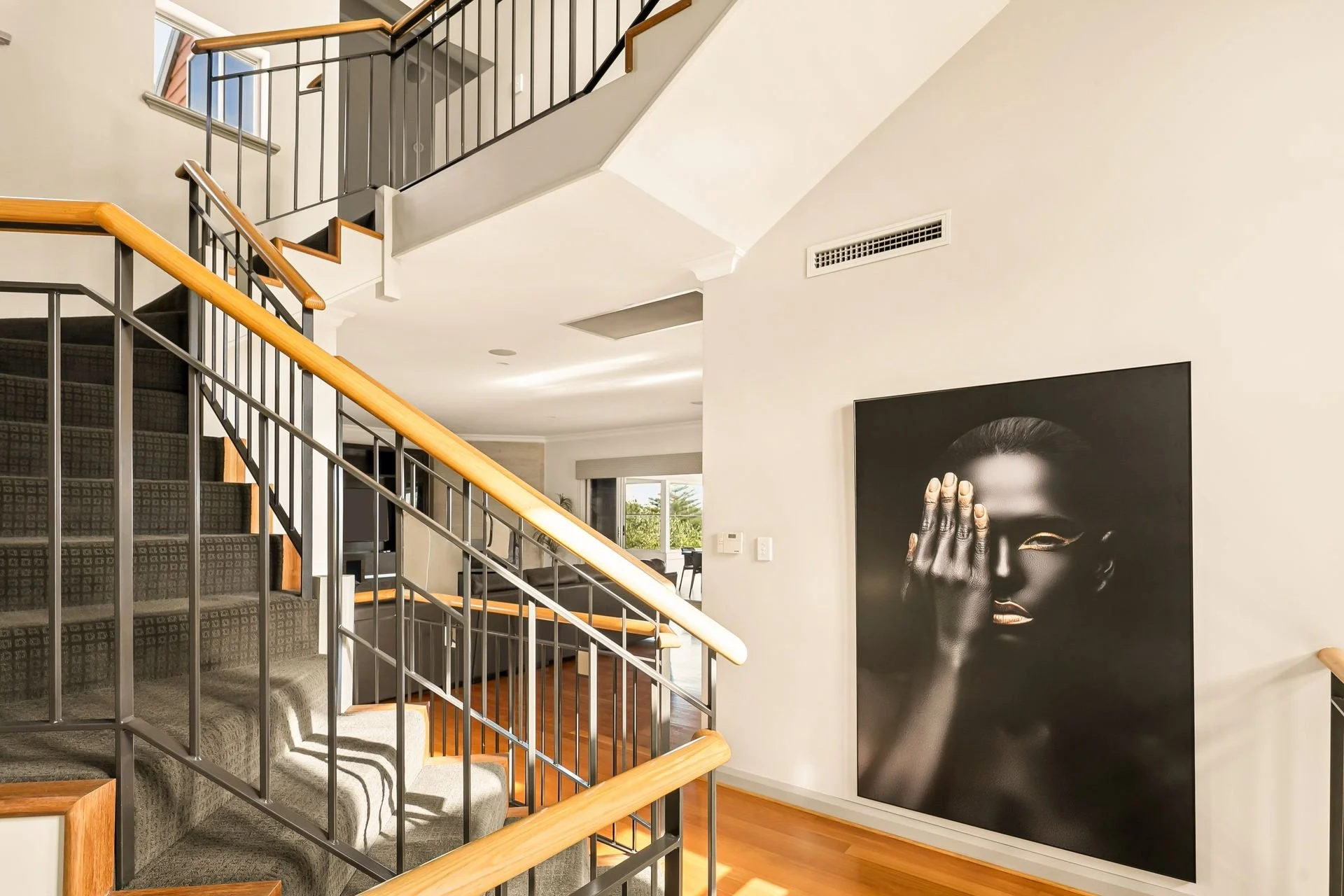 Interior view of a modern home with staircase, artwork, and large windows with natural light.
