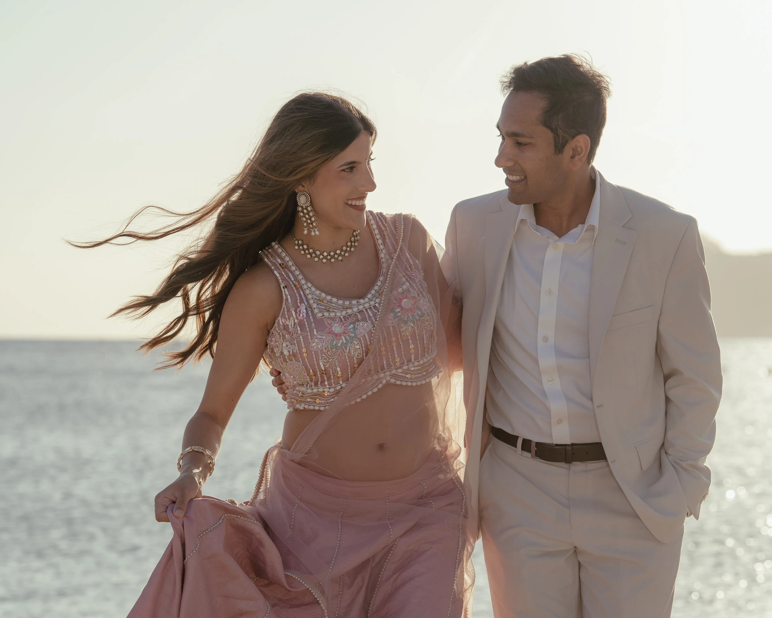 Zwangerschapsshoot op Mallorca met aanstaande ouders die elkaar liefdevol aankijken en glimlachen, terwijl de zwangere vrouw een prachtige roze jurk draagt.