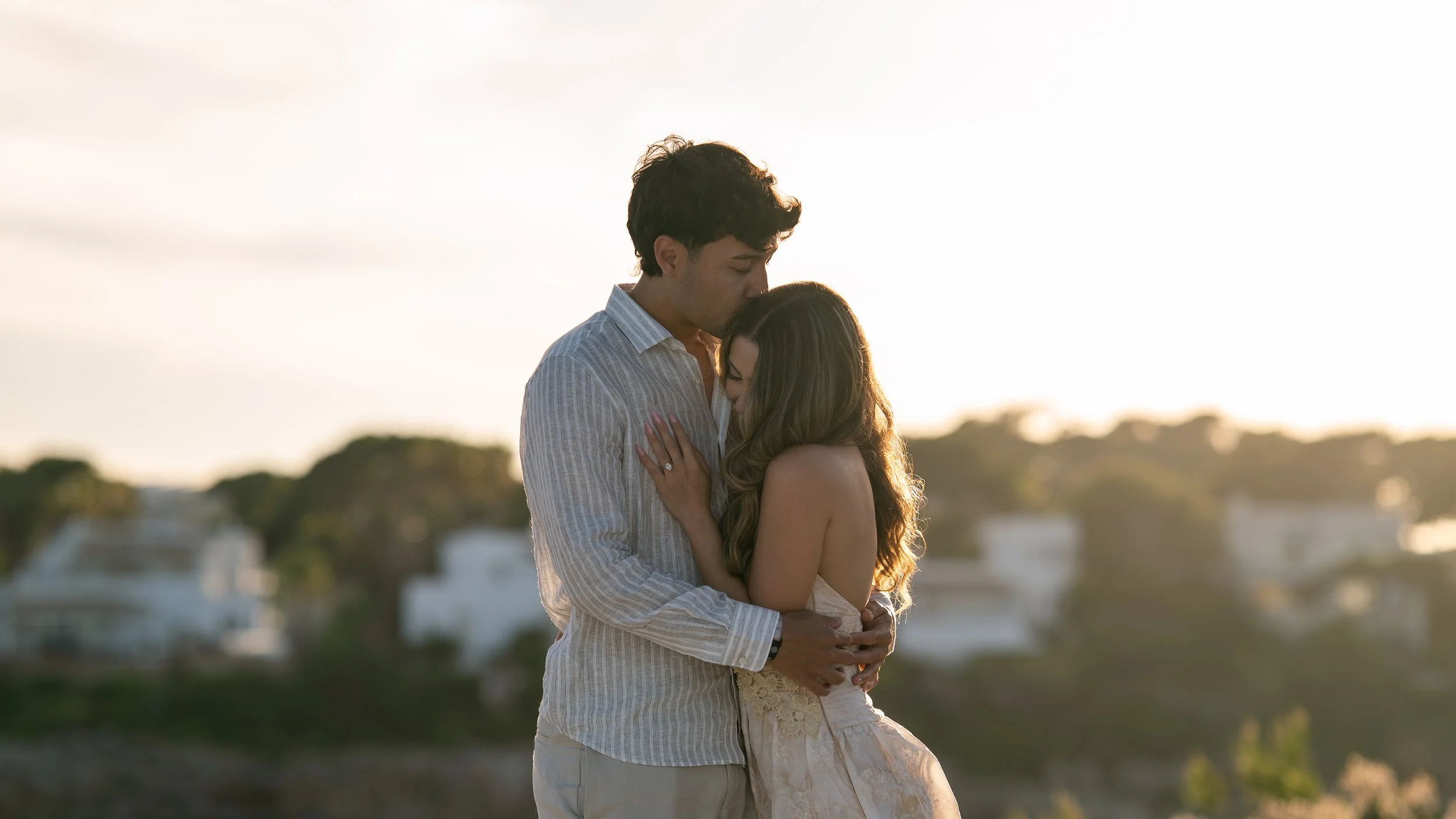 Romantic couple embracing at sunset in Mallorca, with a woman resting in her partner's arms as he gently kisses her head during a natural couples photography session