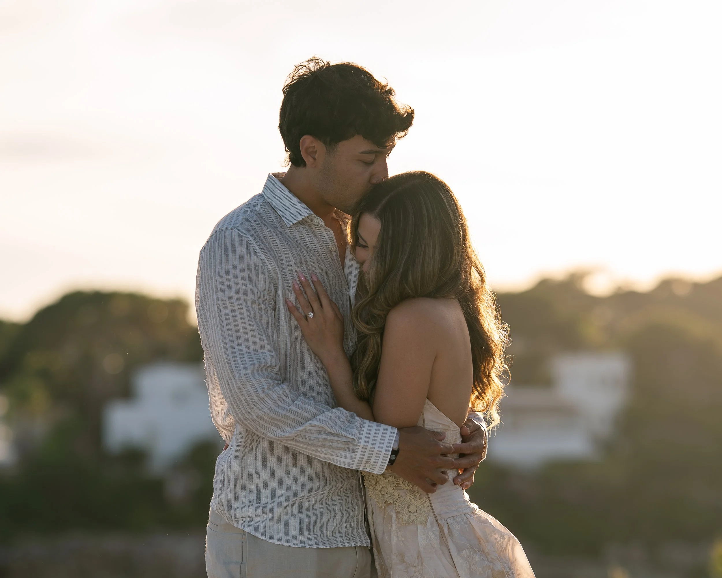 Romantische koppelfotoshoot op Mallorca tijdens zonsondergang, waarbij een man zijn partner liefdevol op haar voorhoofd kust.