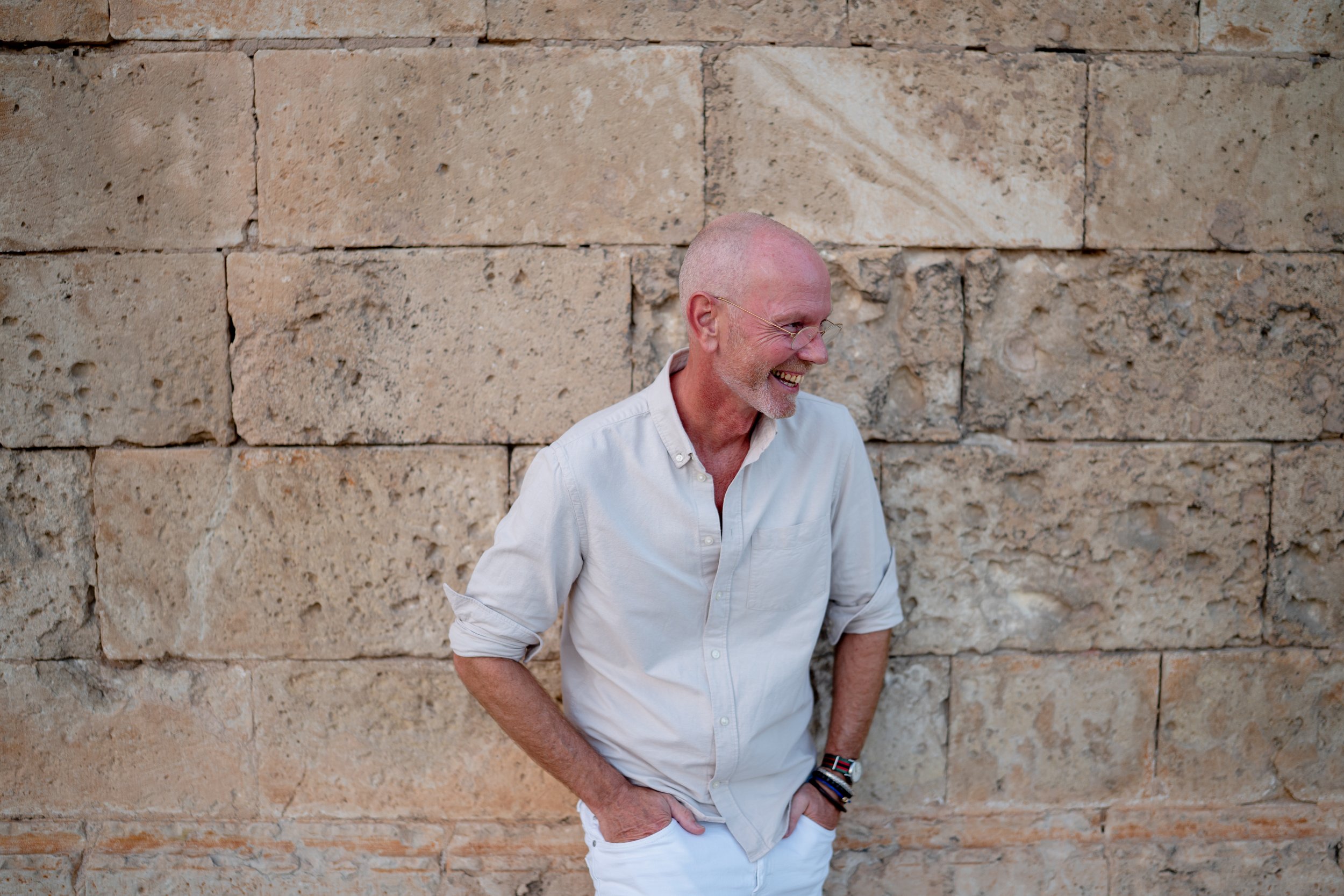 Individuele portretfotoshoot in Palma de Mallorca met een lachende man die ontspannen tegen een muur leunt tijdens een natuurlijke fotosessie in de stad.