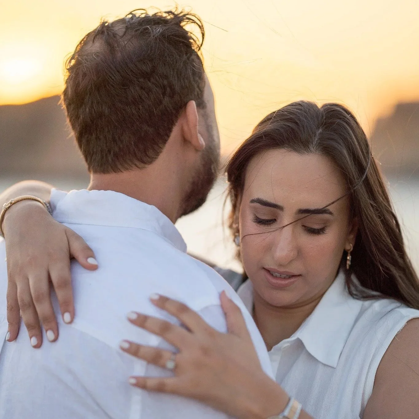 A couple hugging outdoors at sunset, with the woman resting her head on the man's shoulder and her eyes closed in Mallorca