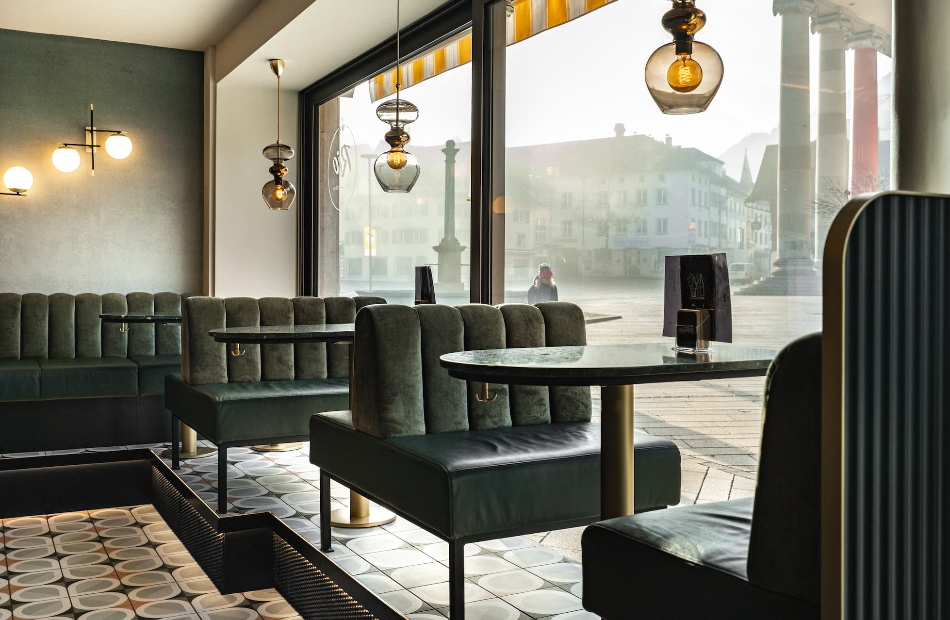 Leere grüne Polsterbank und Tische in einem modern eingerichteten Café mit großen Fenstern, durch die Straßen in der Stadt sichtbar sind.