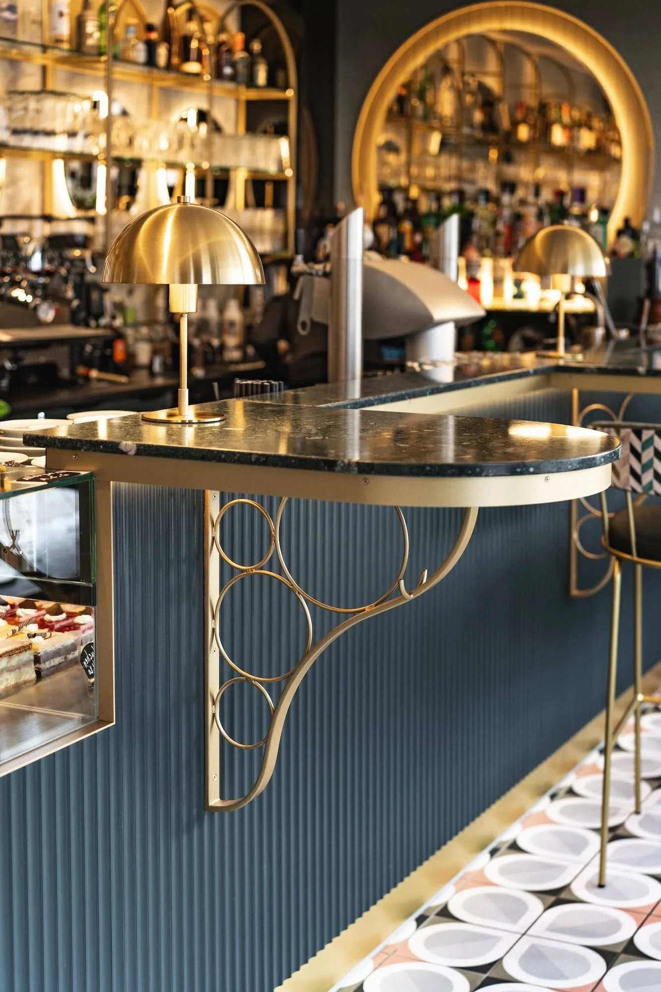 Innenaufnahme der Bar im Rio Café & Cocktailbar in Dornbirn mit schwarzem Steintisch, goldfarbener Lampe und Theke mit Kuchen und Getränken.
