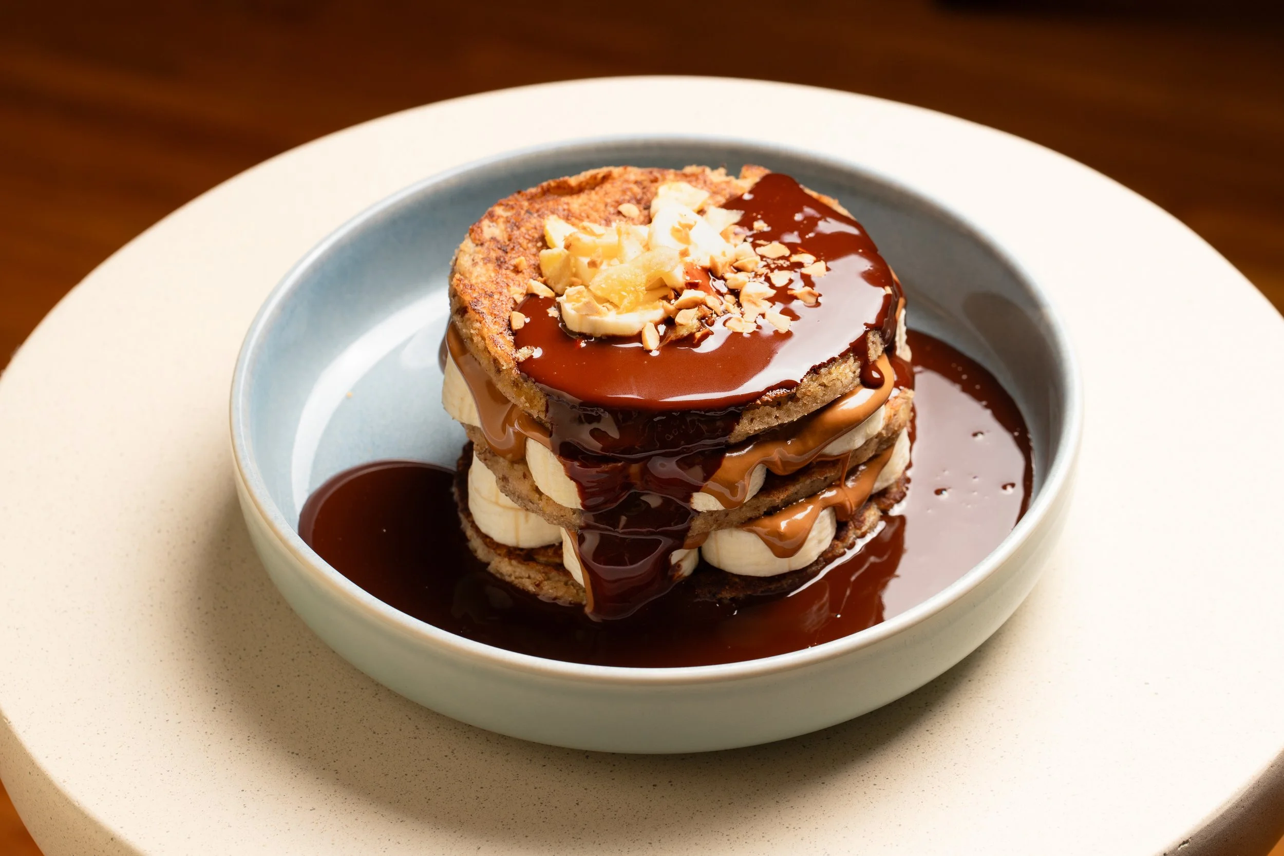 Gluten free chocolate pancakes drizzled with chocolate sauce, peanut butter and topped with chopped nuts, banana.
