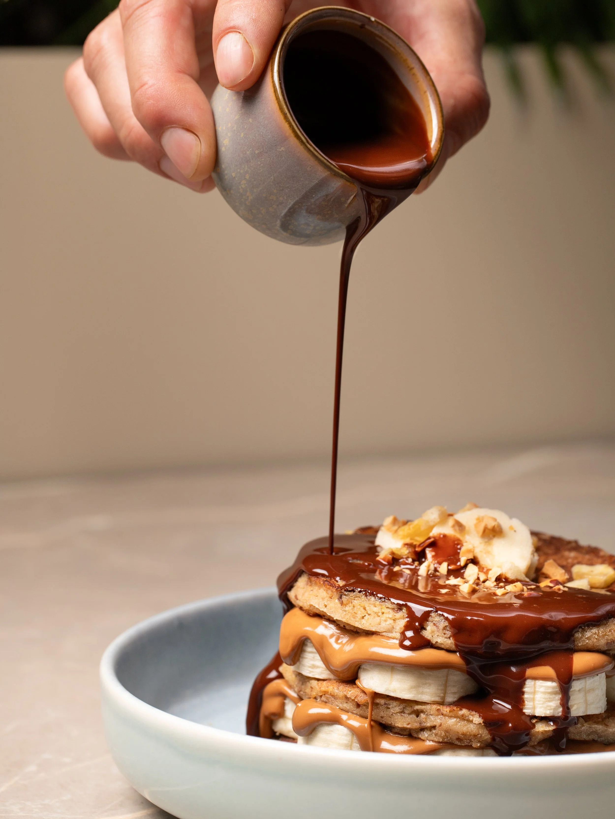 Gluten free, sugar free chocolate pancakes drizzled with chocolate sauce, peanut butter and topped with chopped nuts, banana.
