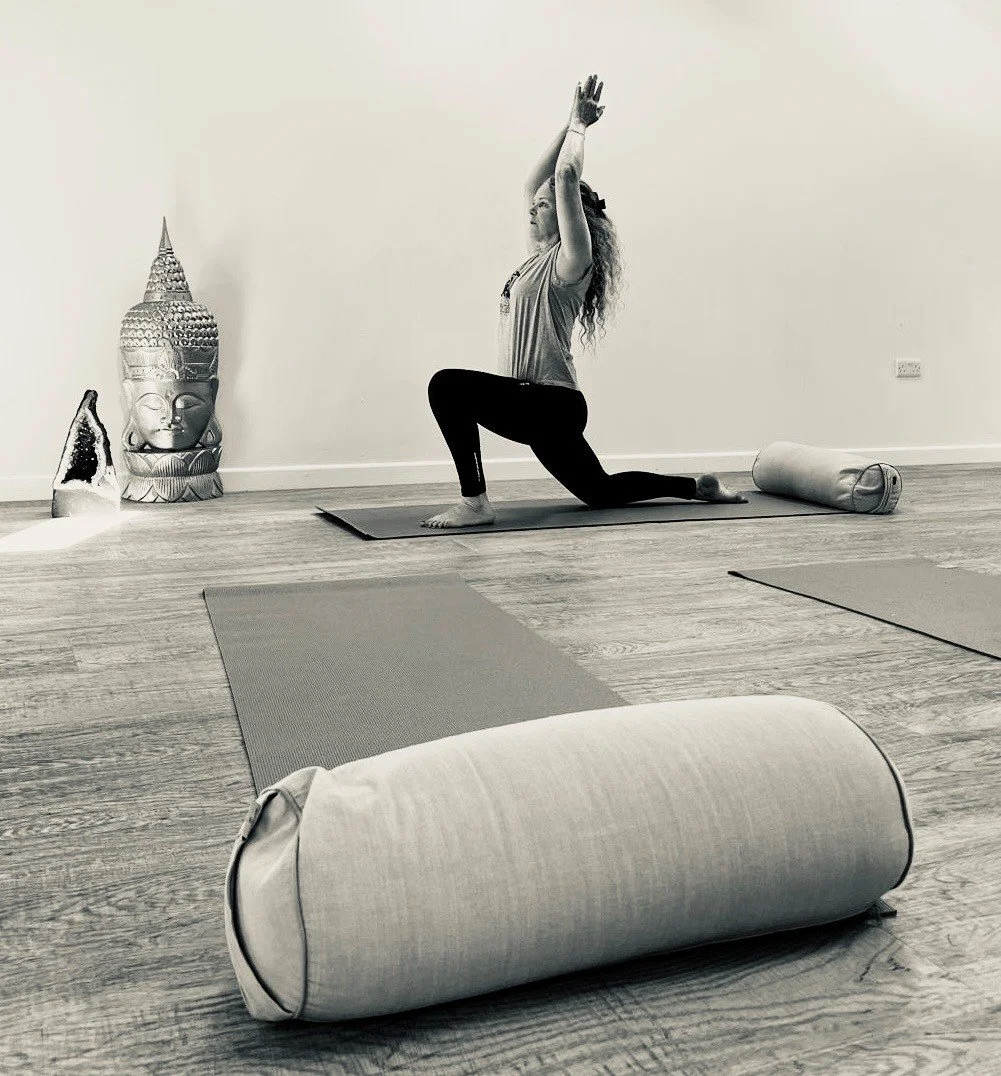 A woman practicing yoga in a room with yoga mats, a large Buddha sculpture, and decorative statues on the floor.