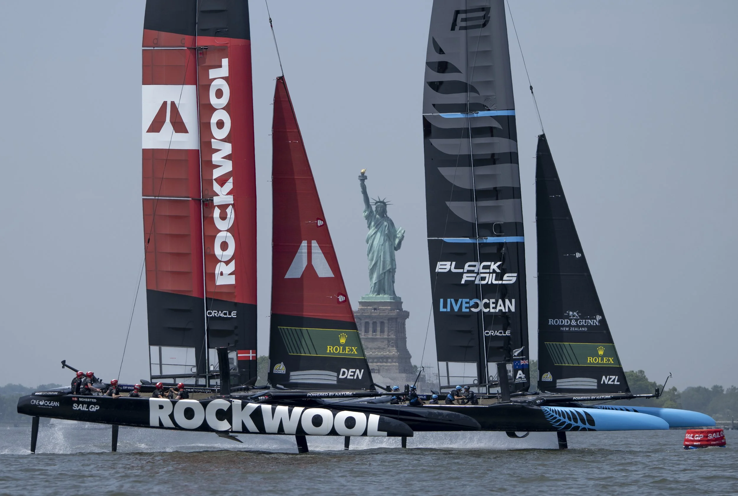 Multiple sailboats racing in a competition with the Statue of Liberty in the background.