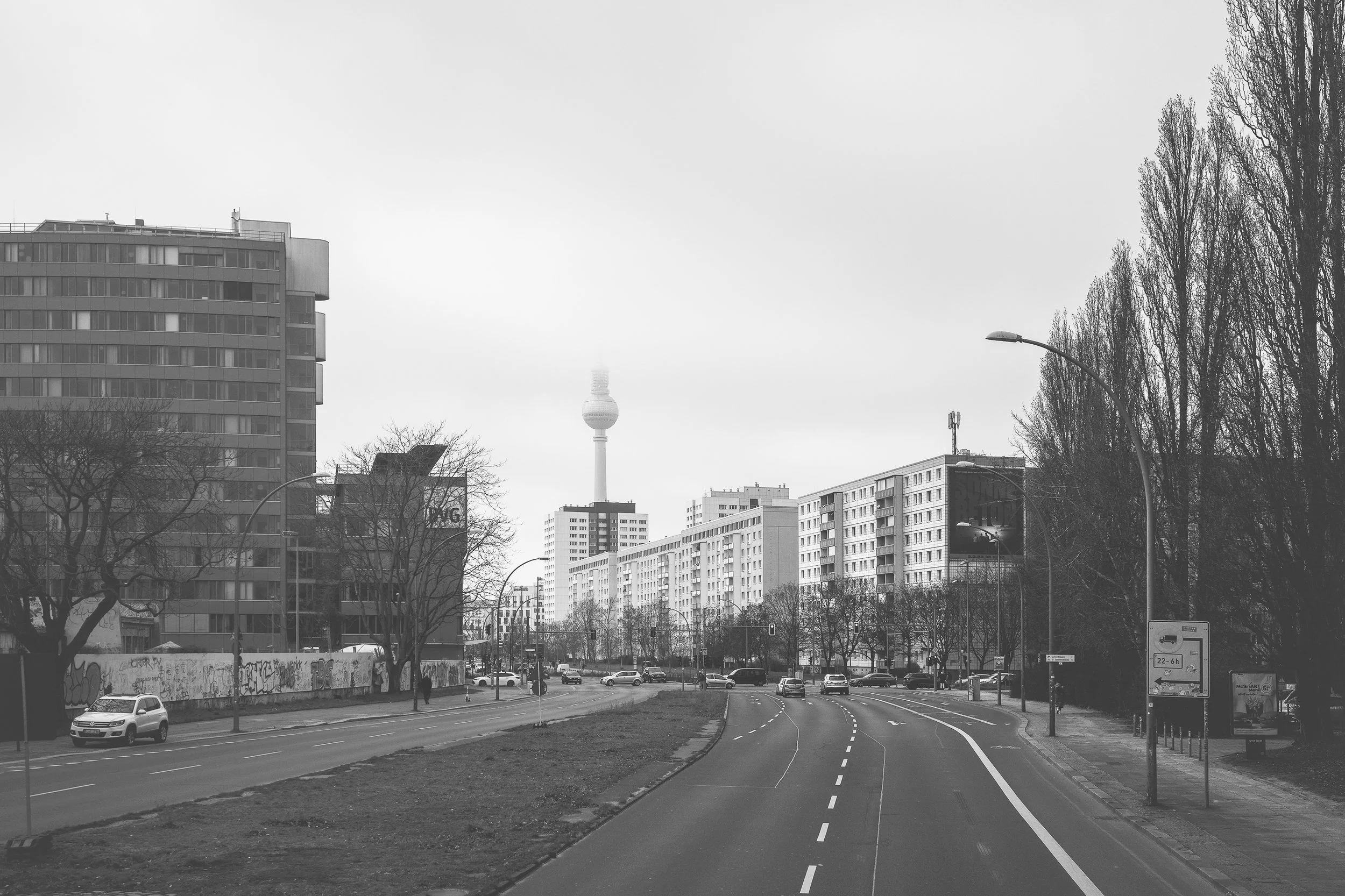 Szeroka ulica w Berlinie z blokami mieszkalnymi - czarno-biała fotografia miasta, perspektywy i powtarzalnej architektury.