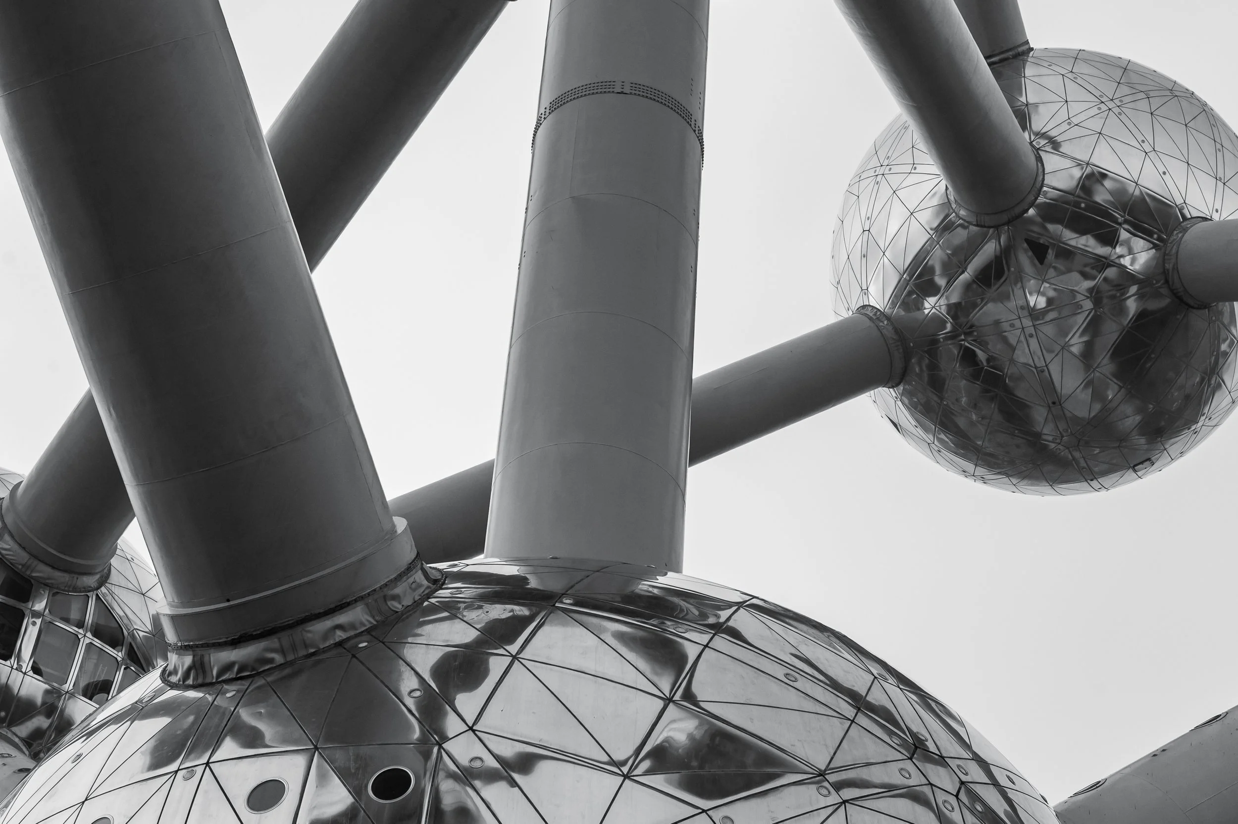 Metalowa kula Atomium w czerni i bieli - detal architektoniczny skupiony na fakturze, świetle i miejskim odbiciu.