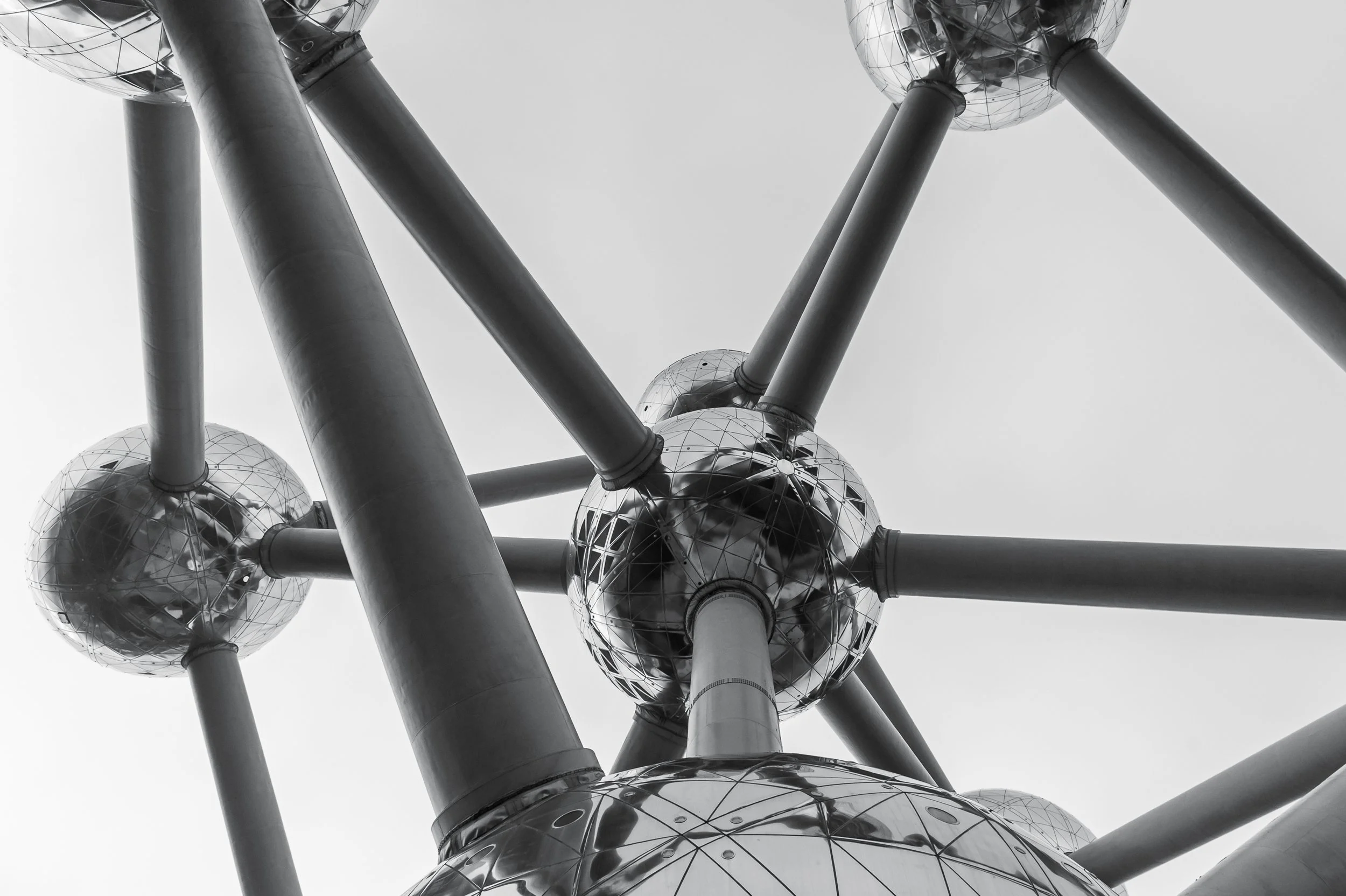 Monumentalny fragment Atomium w Brukseli - fotografia architektury pokazująca ciężar, błysk metalu i futurystyczną formę.