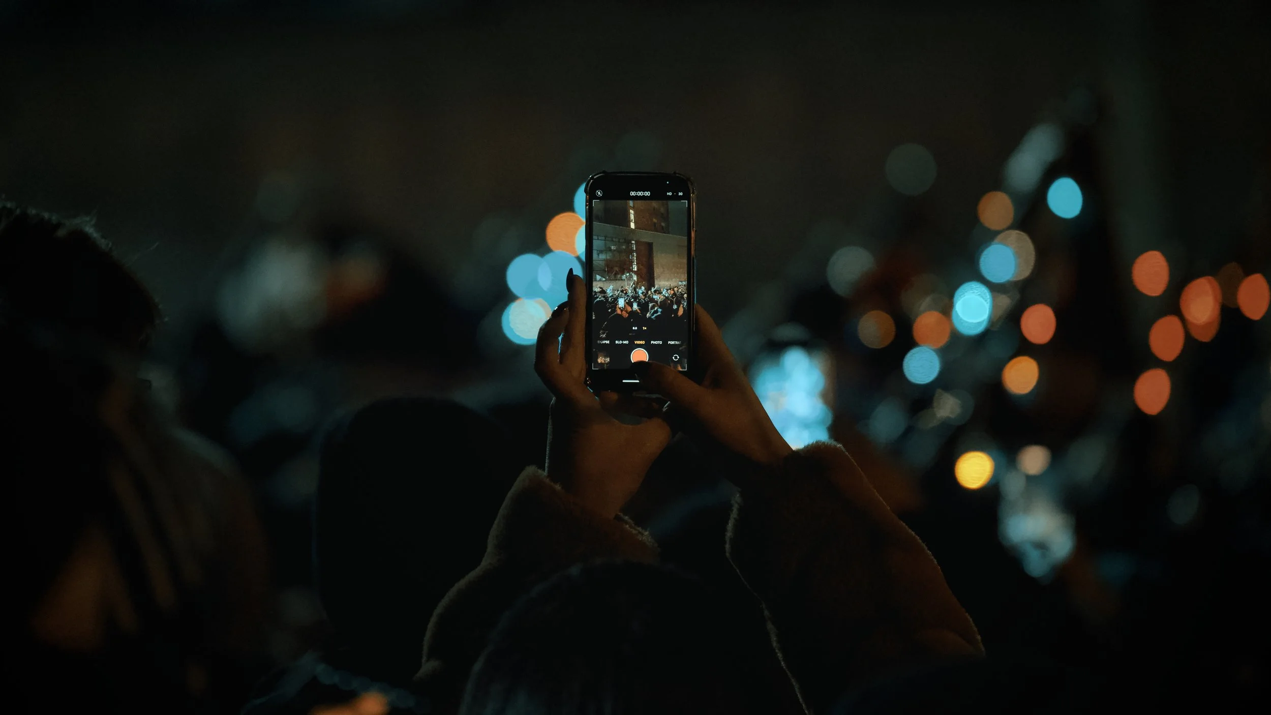 A person holds up their phone to film a Scottish marching band walking along the procession route for Edinburgh's 2025 Hogmanay celebration.