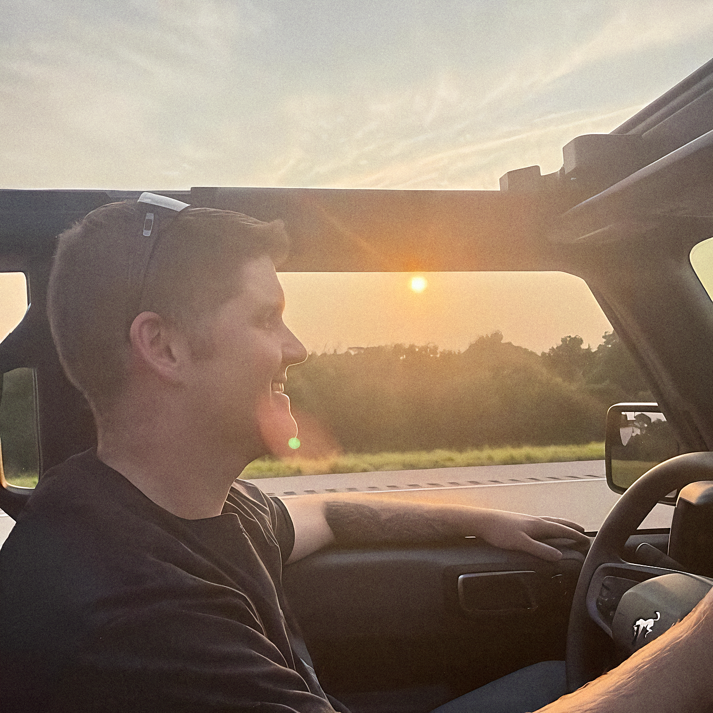 Justin Major driving a car at sunset, smiling and wearing sunglasses on his head.