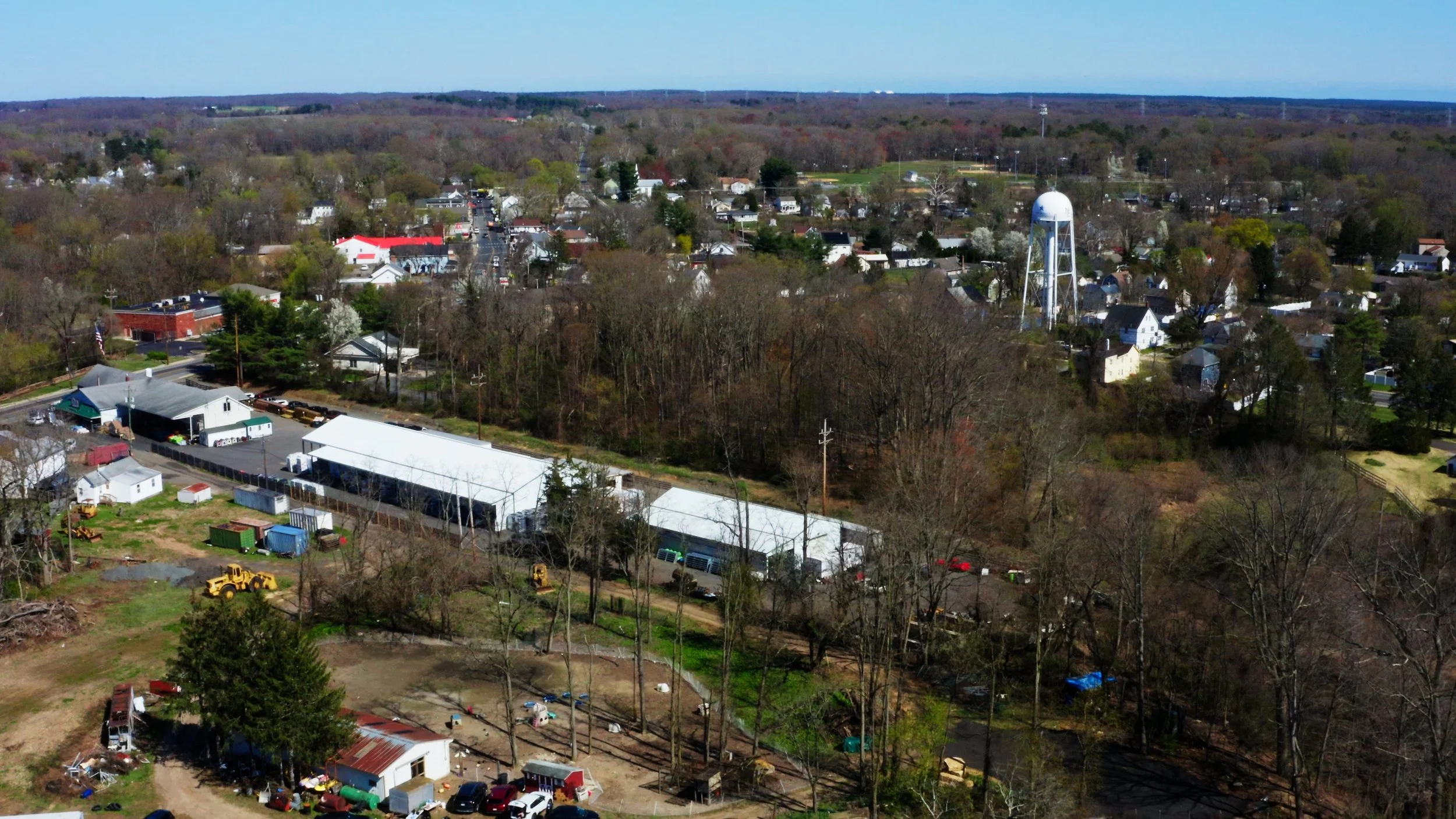 Aerial view of a small town with residential houses, a water tower, commercial buildings, trees, and a clear blue sky.