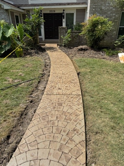 Concrete walkway in front of house with plants and grass on sides, leading to a front door with house number 2026.