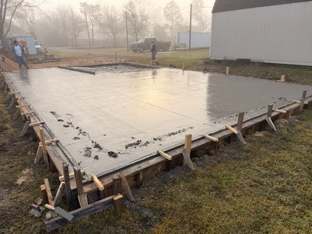 Concrete foundation being poured for a building, with wooden formwork and rebar framing in place.