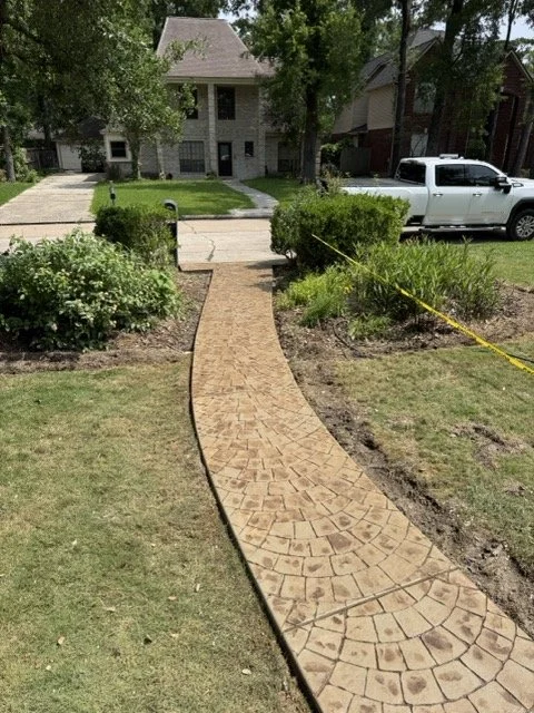 Curved brick sidewalk leading to a house with lush landscaping on both sides and a white truck parked nearby.