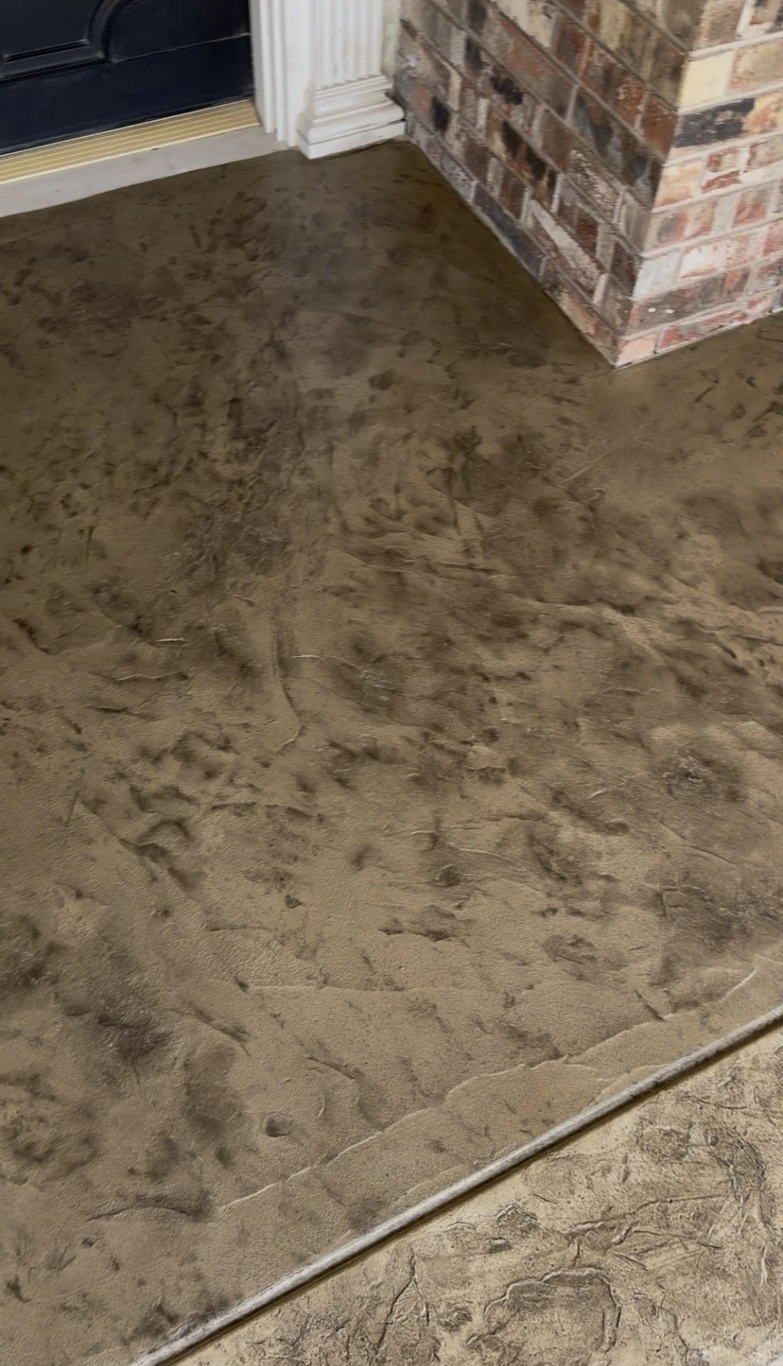 A close-up view of a freshly poured concrete floor next to a brick fireplace and a door with white trim.