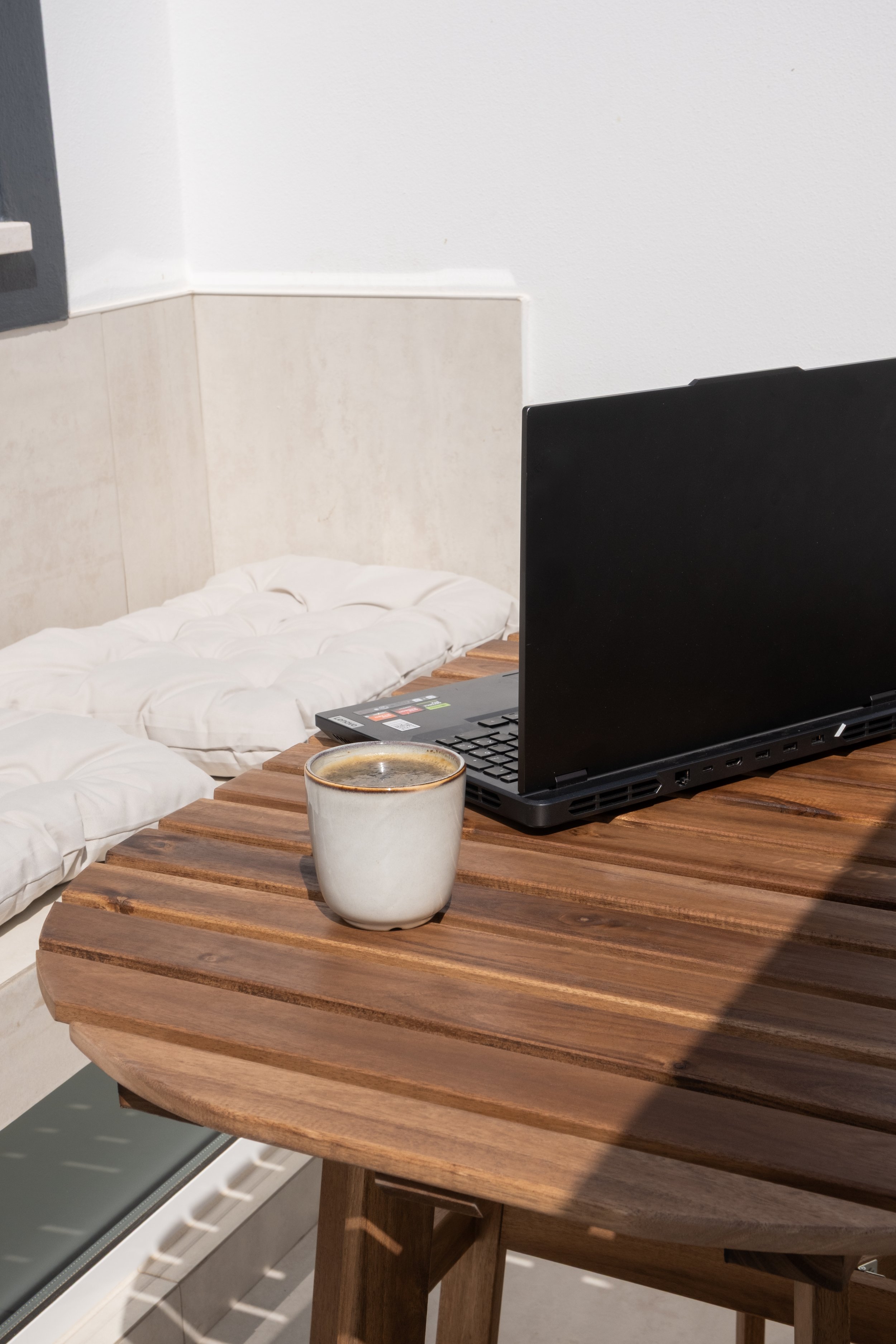 Café em uma xícara sobre mesa de madeira ao lado de um laptop aberto em ambiente interno