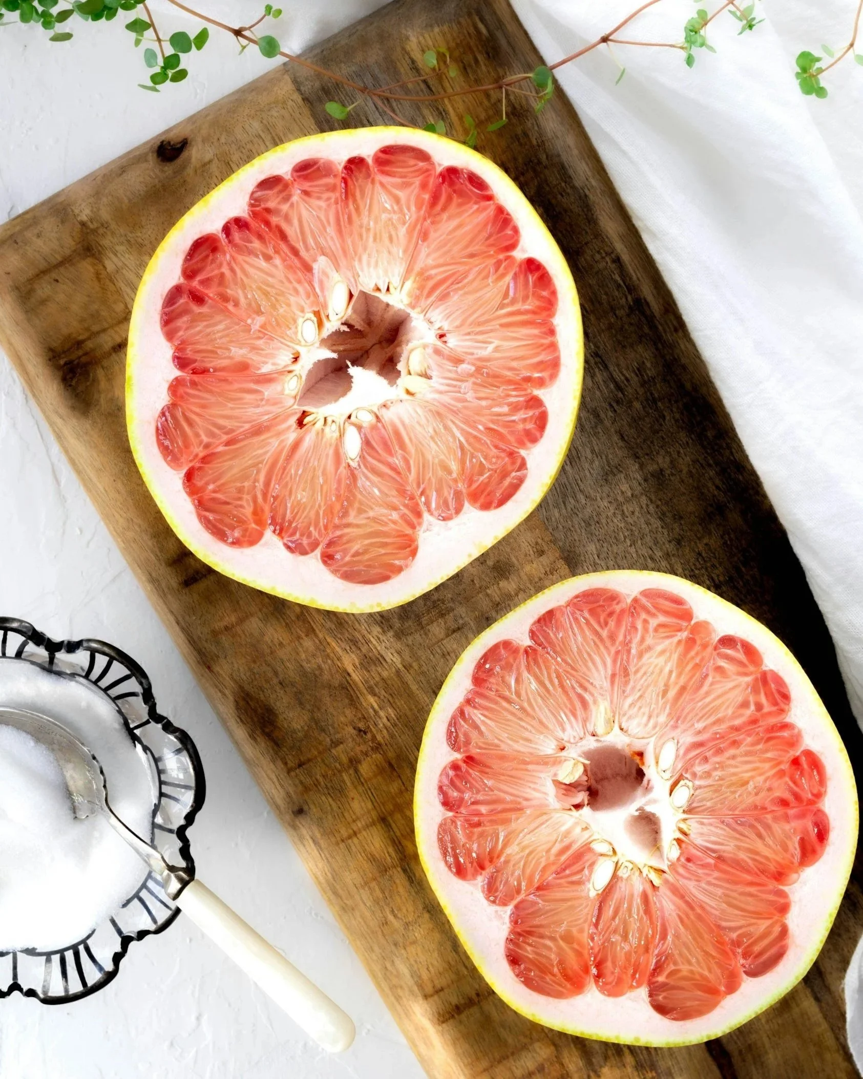 Half of a pink grapefruit on a wooden cutting board with a white cloth and salt shaker nearby.