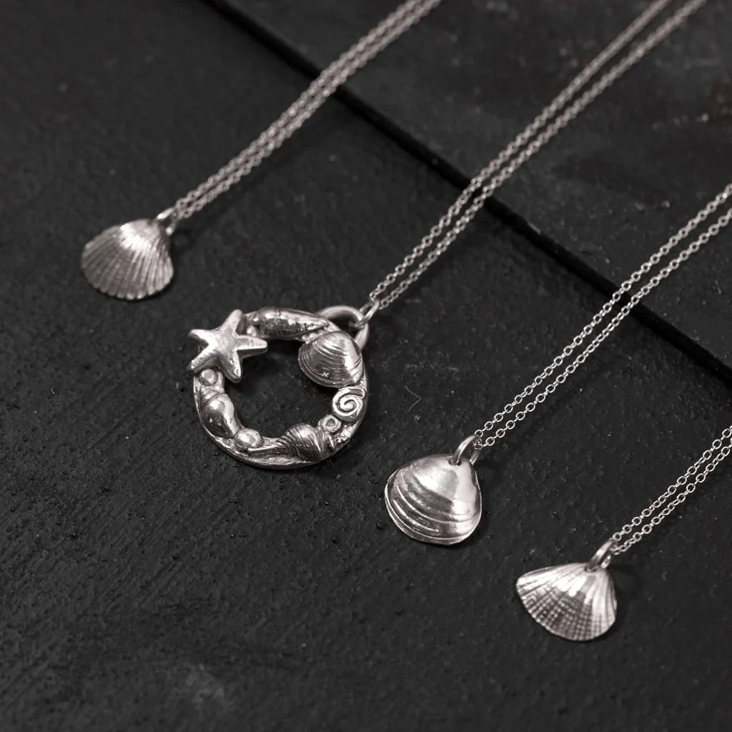 Four silver necklaces with seashell and starfish pendants displayed on a black surface.