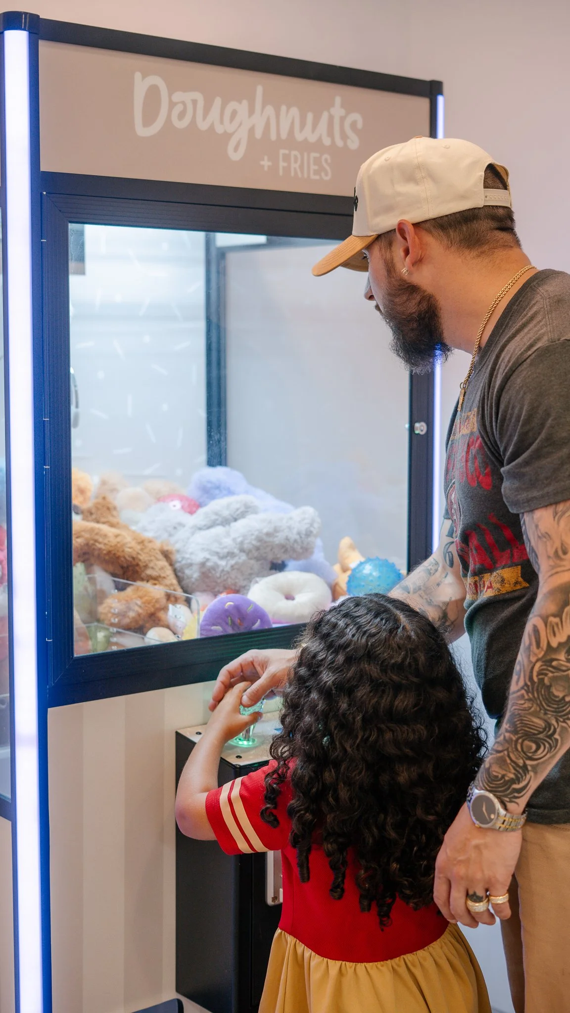 A man and a young girl playing a claw machine filled with plush toys at a arcade or game center.