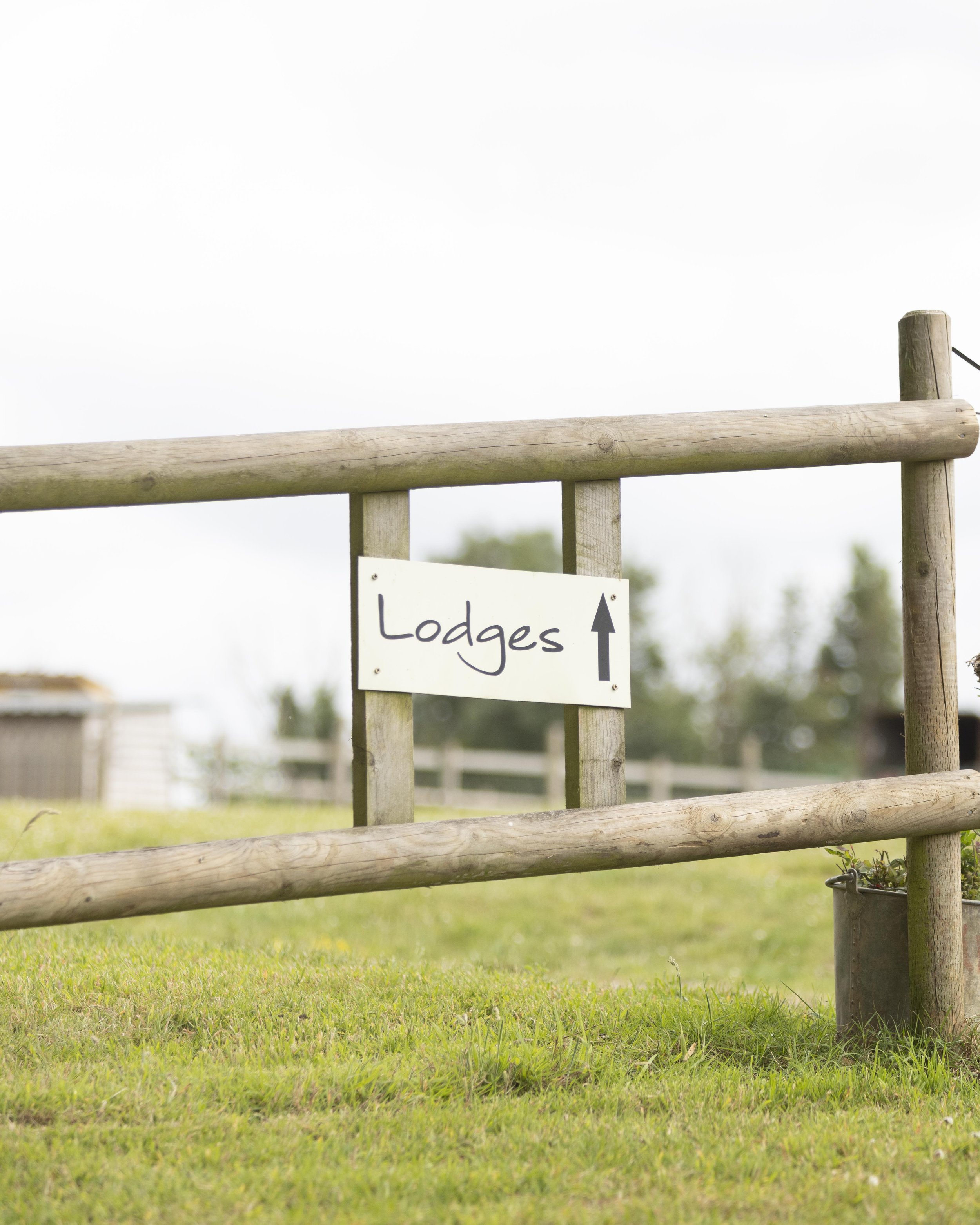 Wooden entrance gate with a sign pointing towards lodges, surrounded by green grass