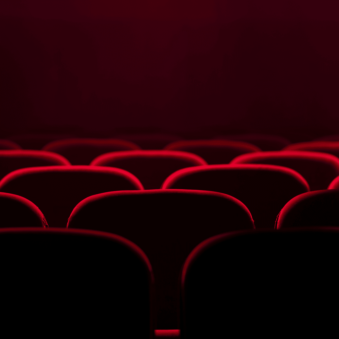Empty theater with rows of red-lit seats, dark background.