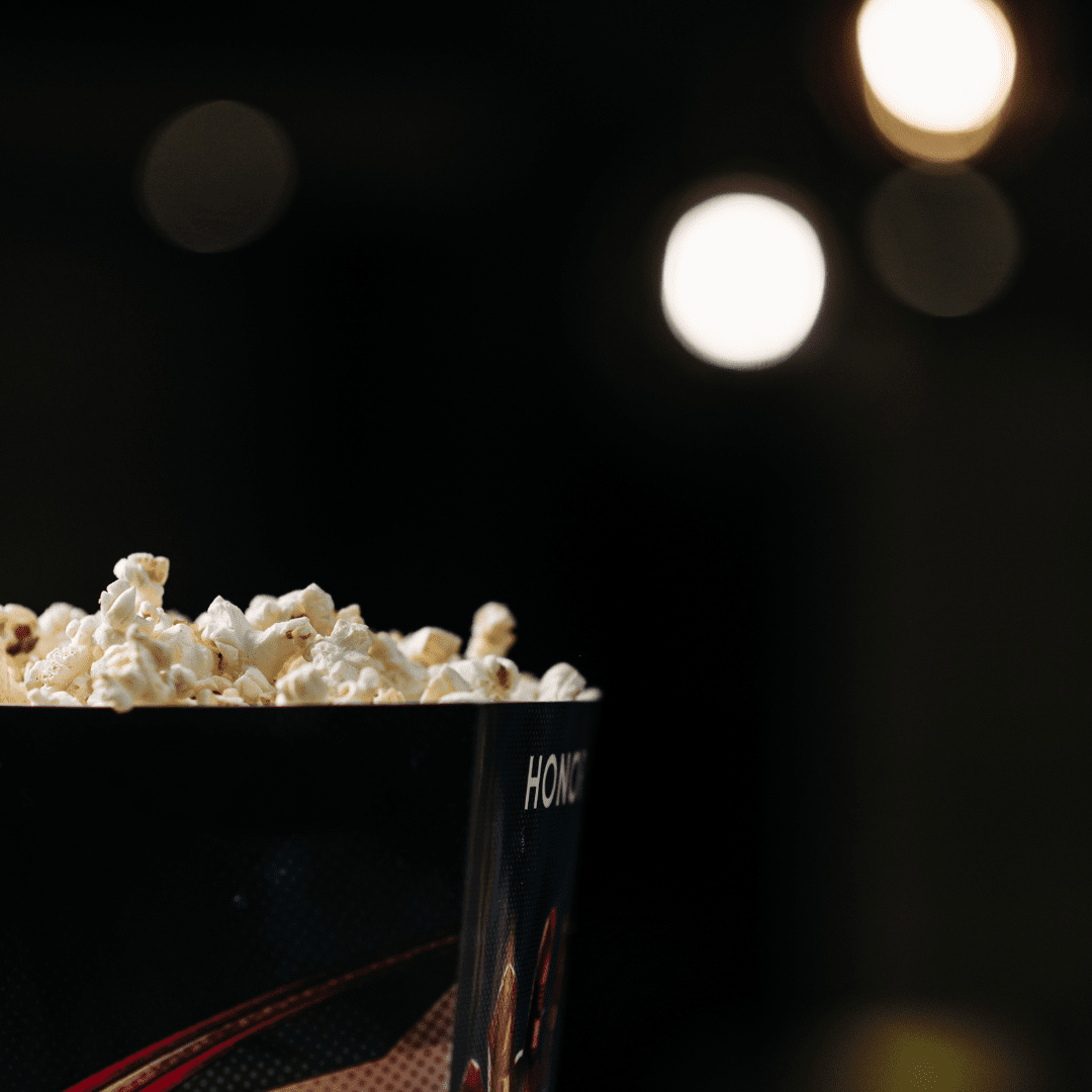 A bucket of popcorn with a dark background and blurred lights in the distance.